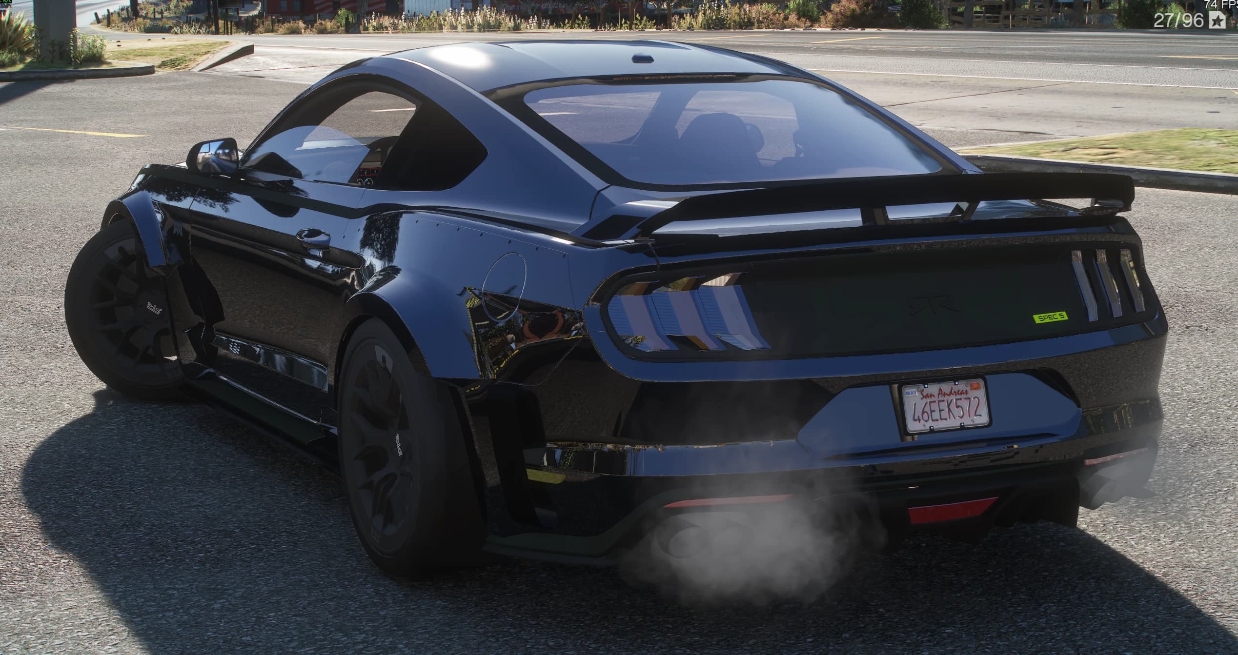 Tres cuartos trasero del Mustang negro con el alerón alto, el distintivo verde SPEC 5 en el portón, el rótulo RTR, los pilotos de tres barras y humo saliendo de la cuádruple salida de escape