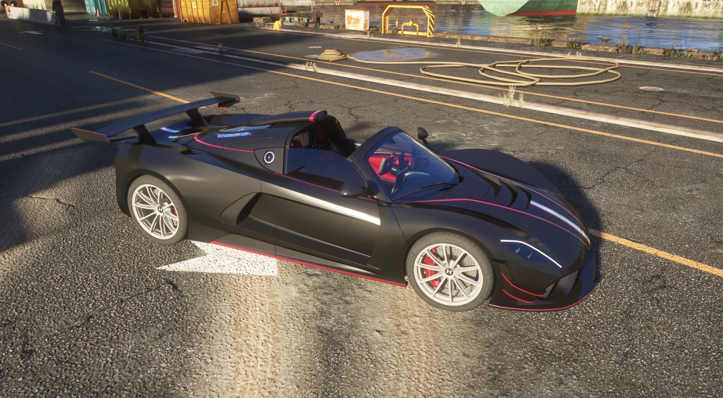 Vista en picado del Venom F5 Roadster de carbono negro con el habitáculo descubierto, interior rojo y alerón trasero de cuello de cisne, en un muelle