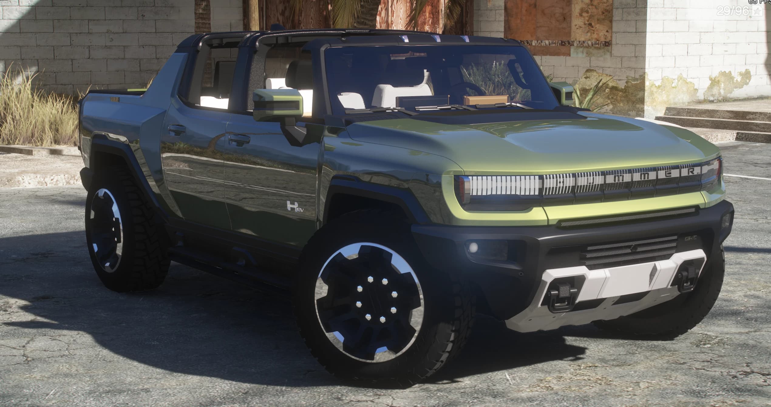 GMC Hummer EV pickup en verde bitono con los paneles del techo quitados, aparcado junto a un edificio de ladrillo abandonado, con la parrilla luminosa HUMMER y ruedas de taco