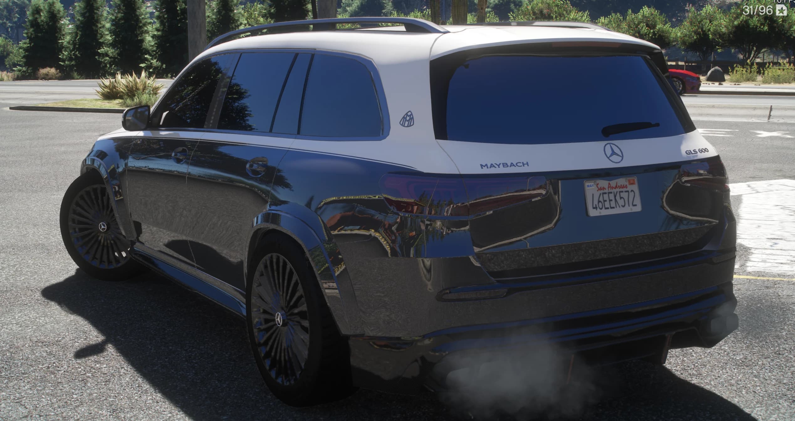 Vista trasera en tres cuartos junto a una carretera arbolada con las letras MAYBACH y GLS 600 en el portón, el emblema Maybach en el pilar y humo del escape