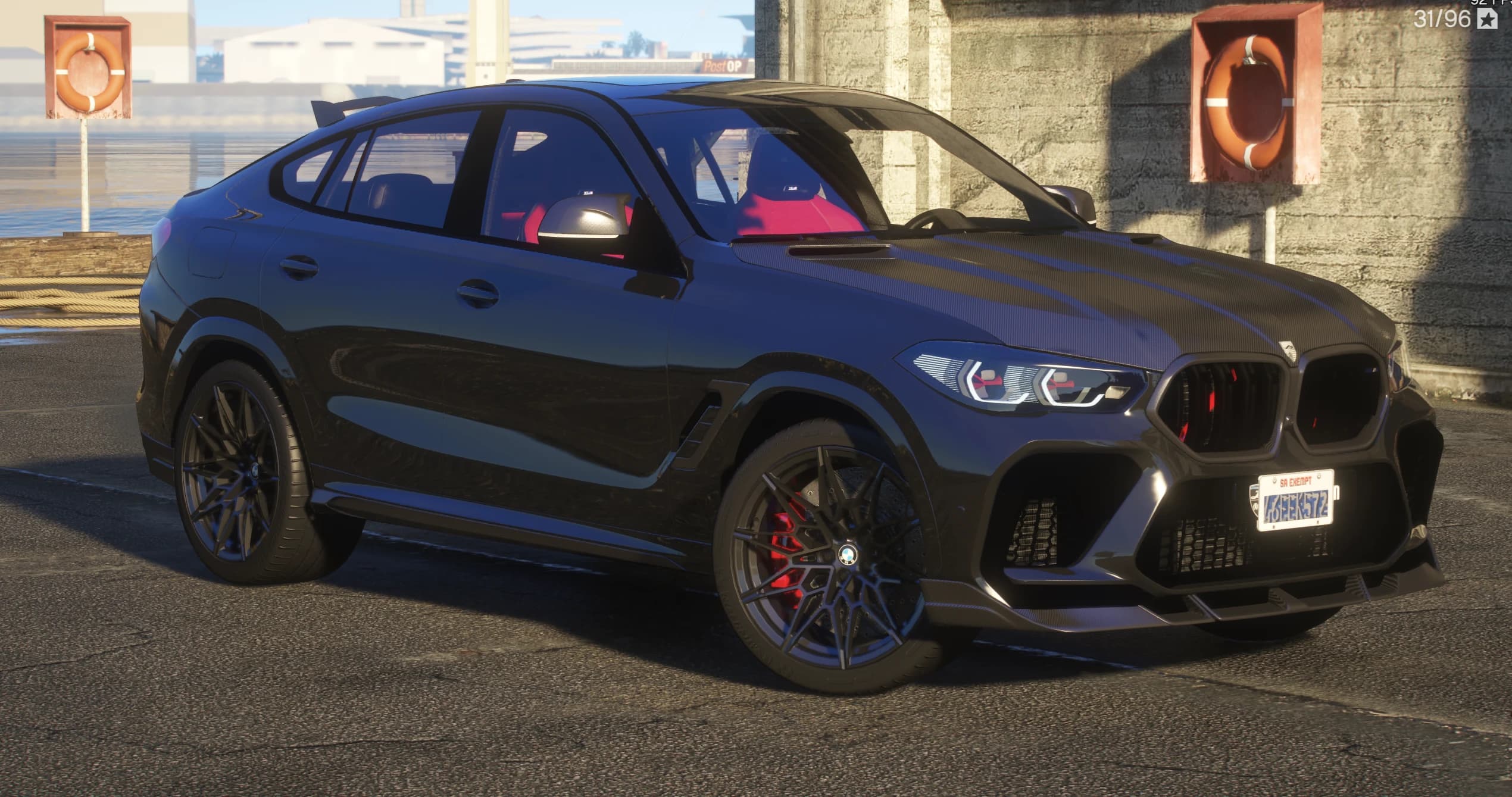 Vista frontal en tres cuartos del BMW X6M negro con el capó de carbono, las parrillas con detalles rojos, el splitter delantero de carbono y los asientos deportivos rojos visibles tras el cristal, aparcado en los muelles