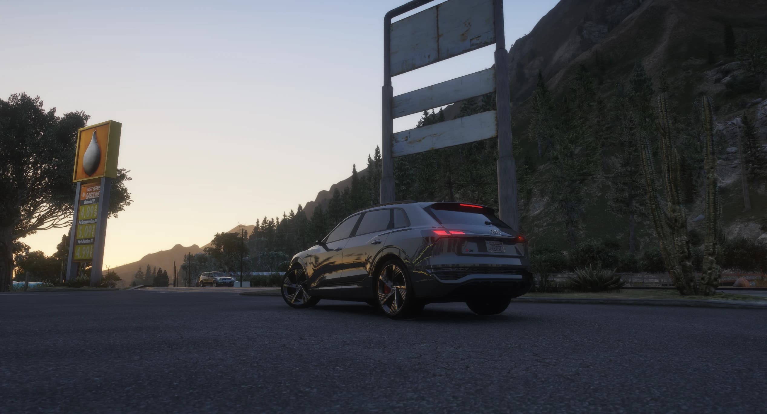 Ángulo trasero bajo del Q8 E-Tron aparcado junto al cartel de precios de una gasolinera rural al anochecer, con las montañas y los cactus de Blaine County al fondo