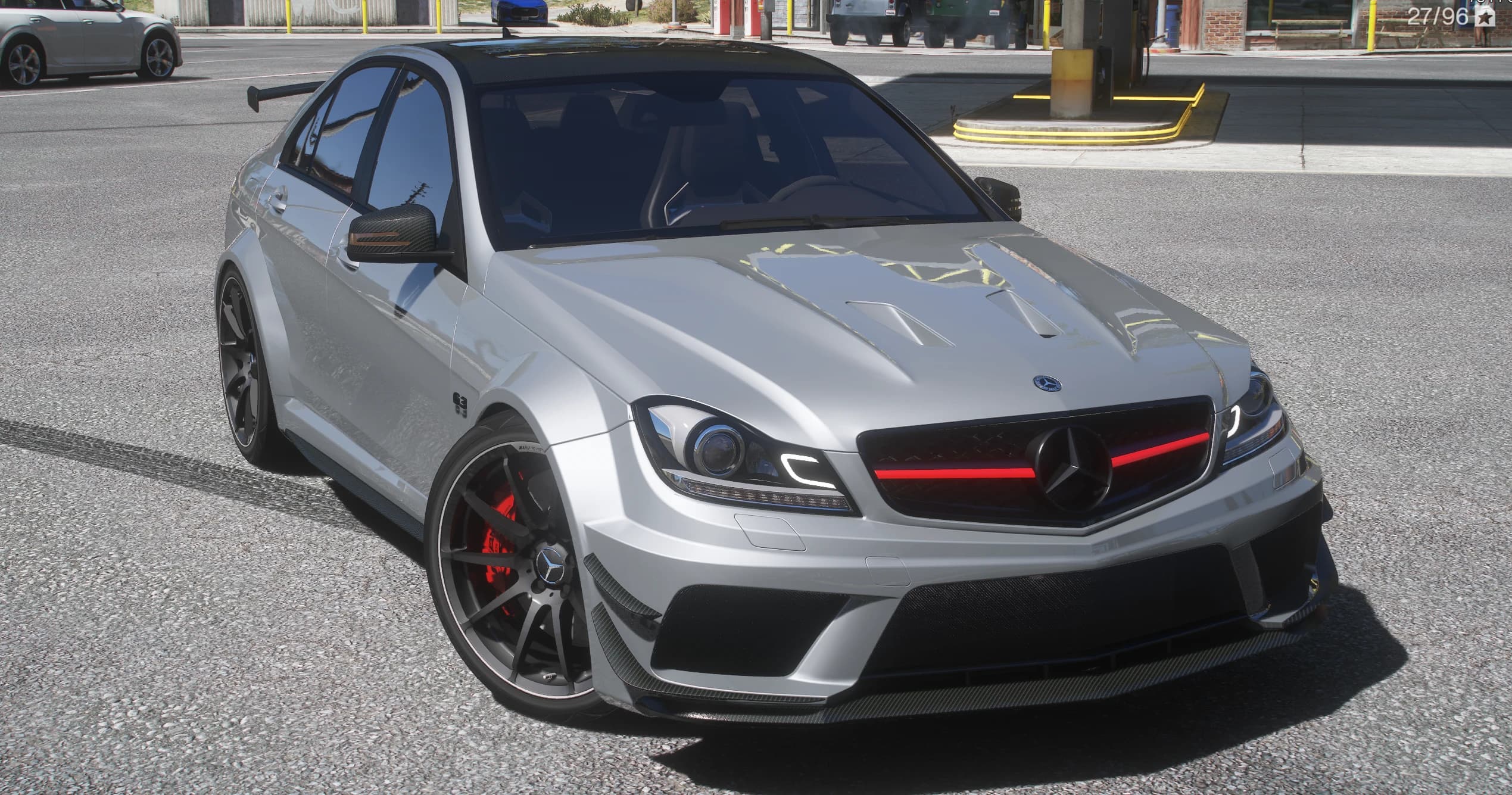 Mercedes-Benz C63 AMG W204 Black Series widebody en plata, vista frontal en tres cuartos con los pasos de rueda ensanchados y ventilados, el splitter de carbono, la parrilla oscura de malla con su barra roja y llantas negras sobre pinzas de freno rojas