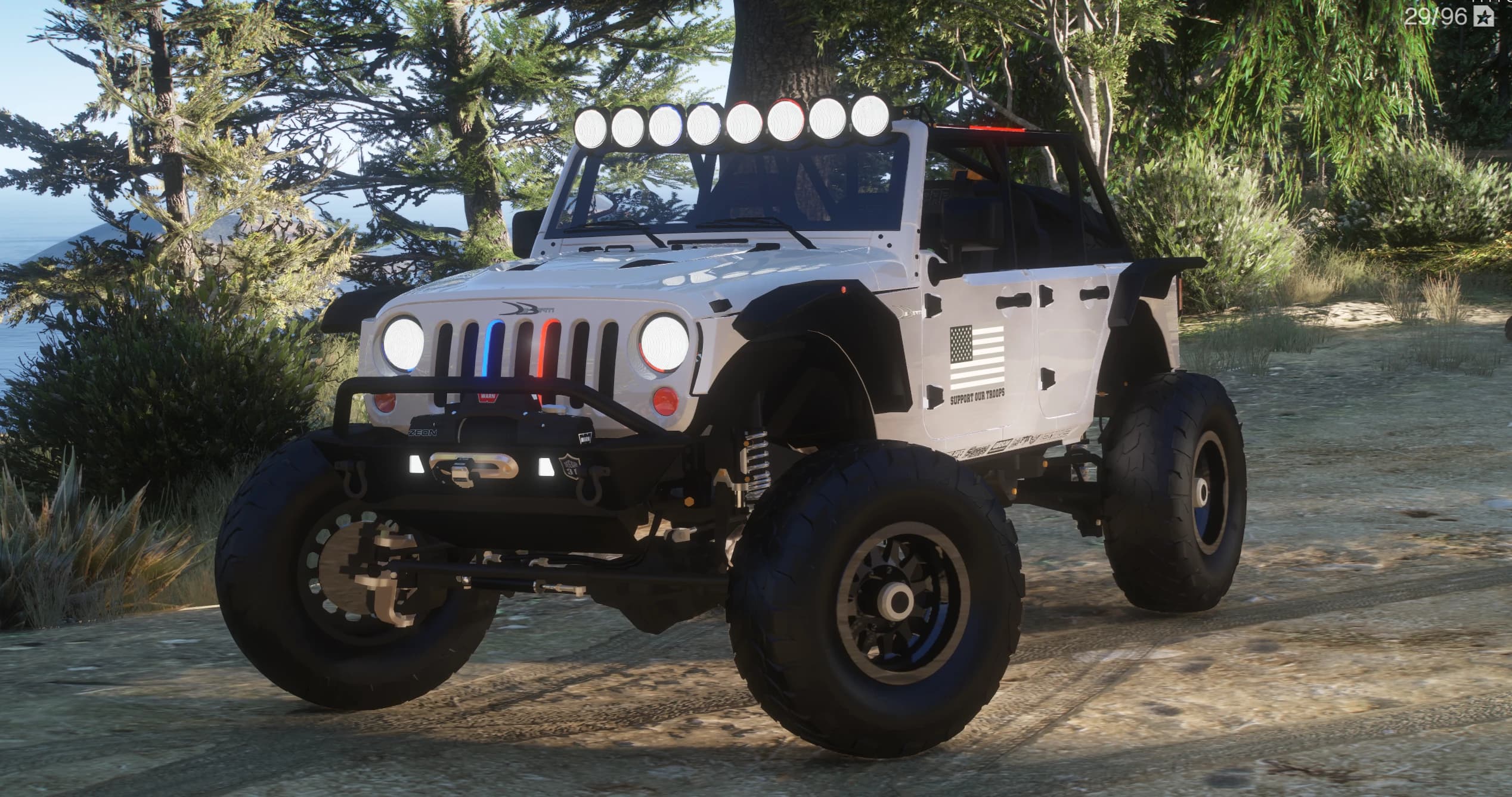 El mismo Wrangler blanco a la luz del día en un camino de tierra, tres cuartos frontal, mostrando la barra de focos, el parachoques con cabrestante y las luces rojas y azules de la parrilla