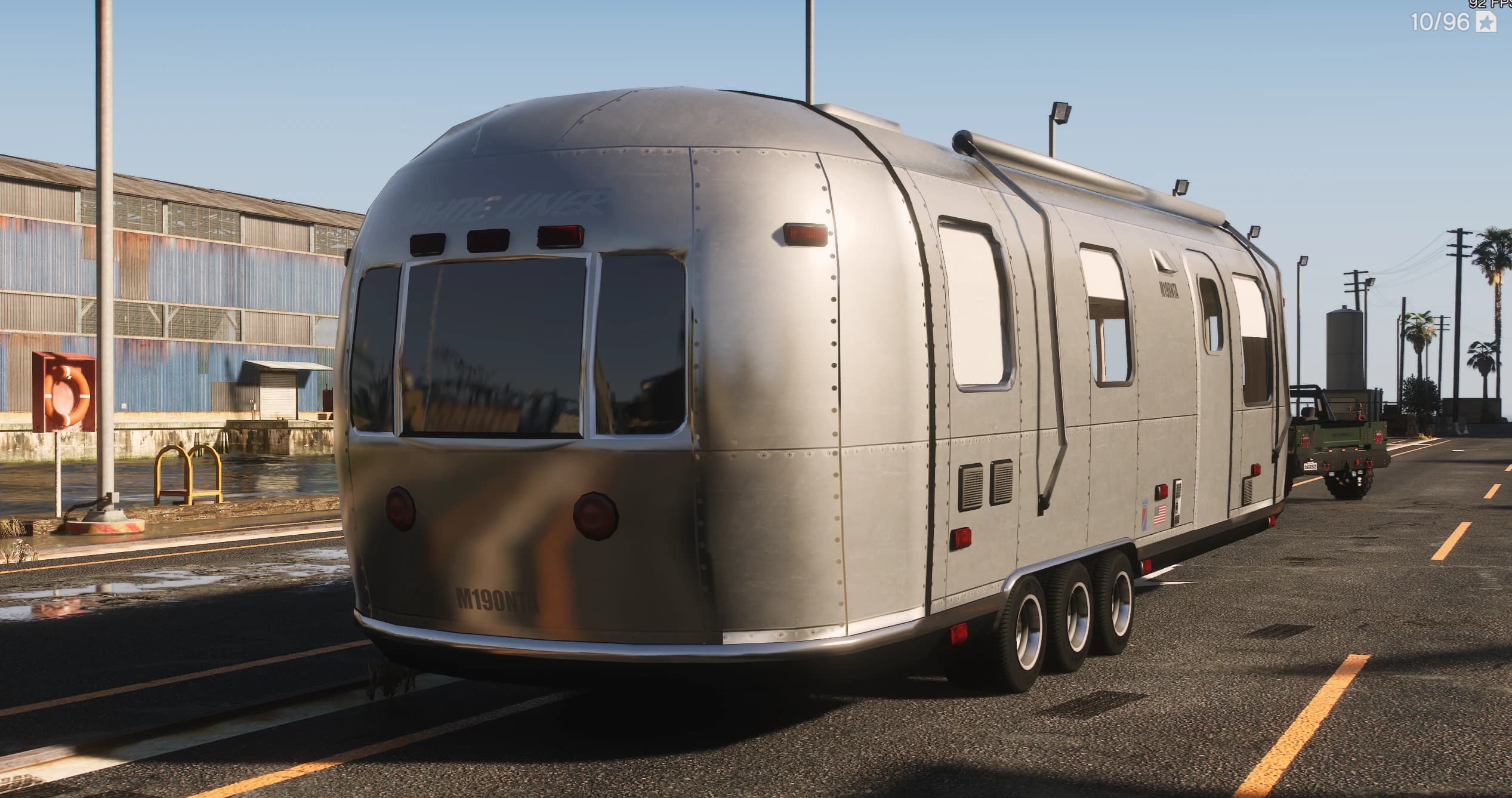 Tres cuartos trasero de la caravana White Liner plateada con el extremo redondeado, los pilotos y la matrícula M190NTB junto a una nave
