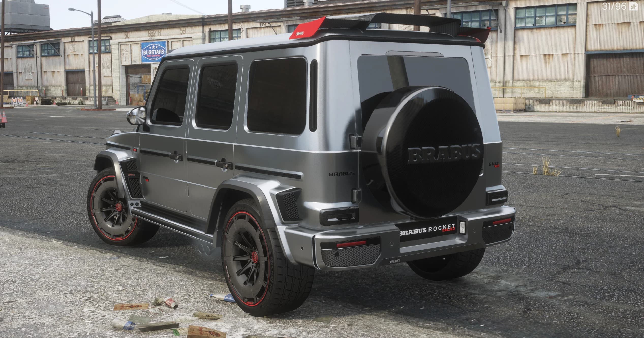 Vista trasera en tres cuartos con la funda de carbono de la rueda de repuesto con letras Brabus, el alerón de techo con punta roja, los emblemas GV12 y las llantas con filo rojo