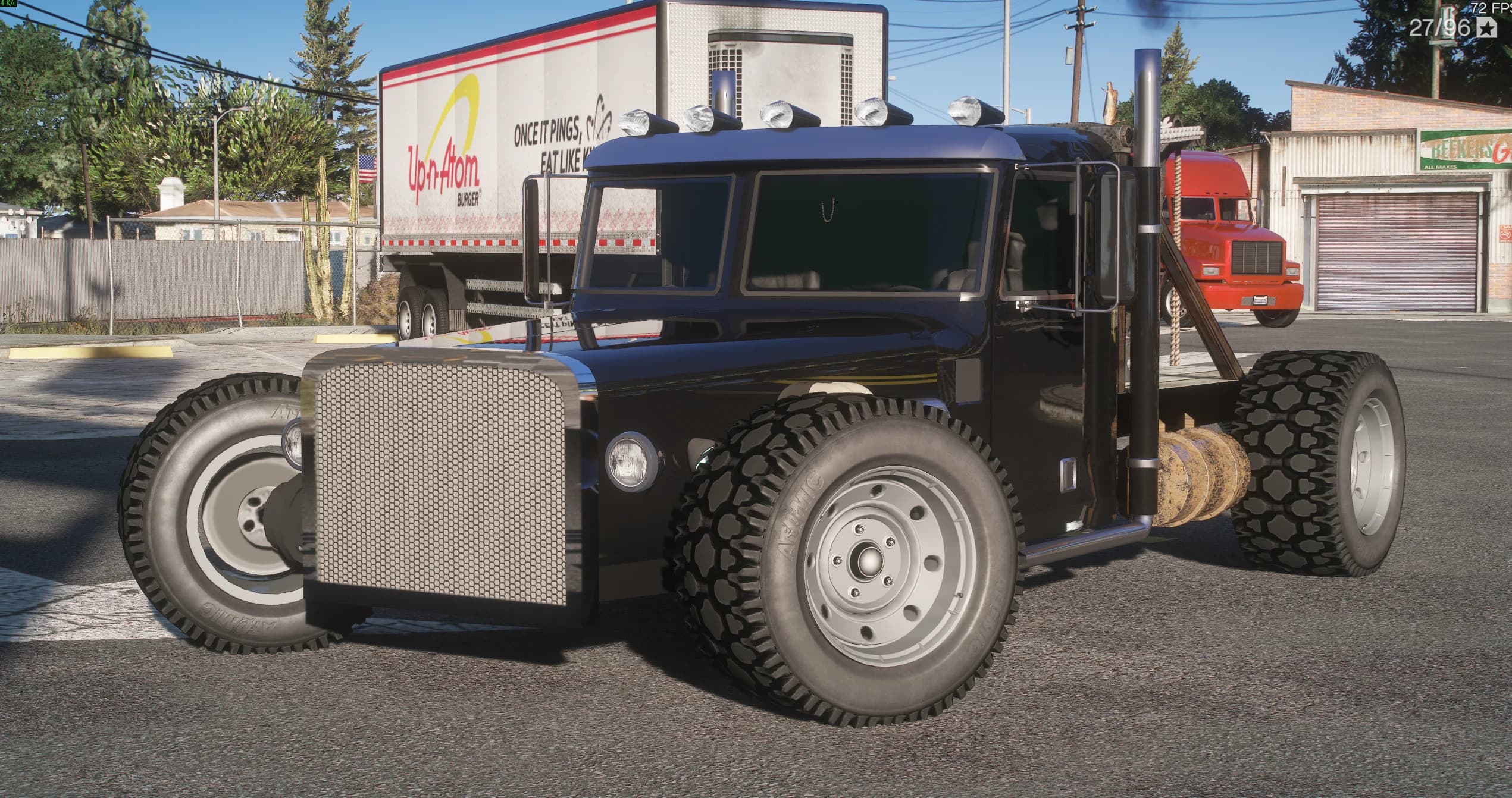 Peterbilt Tow-Rod negro en una explanada industrial, vista frontal en tres cuartos con la cabina recortada, la parrilla cromada de malla, los cinco pilotos sobre el techo, los dos tubos de escape cromados y los neumáticos de tacos