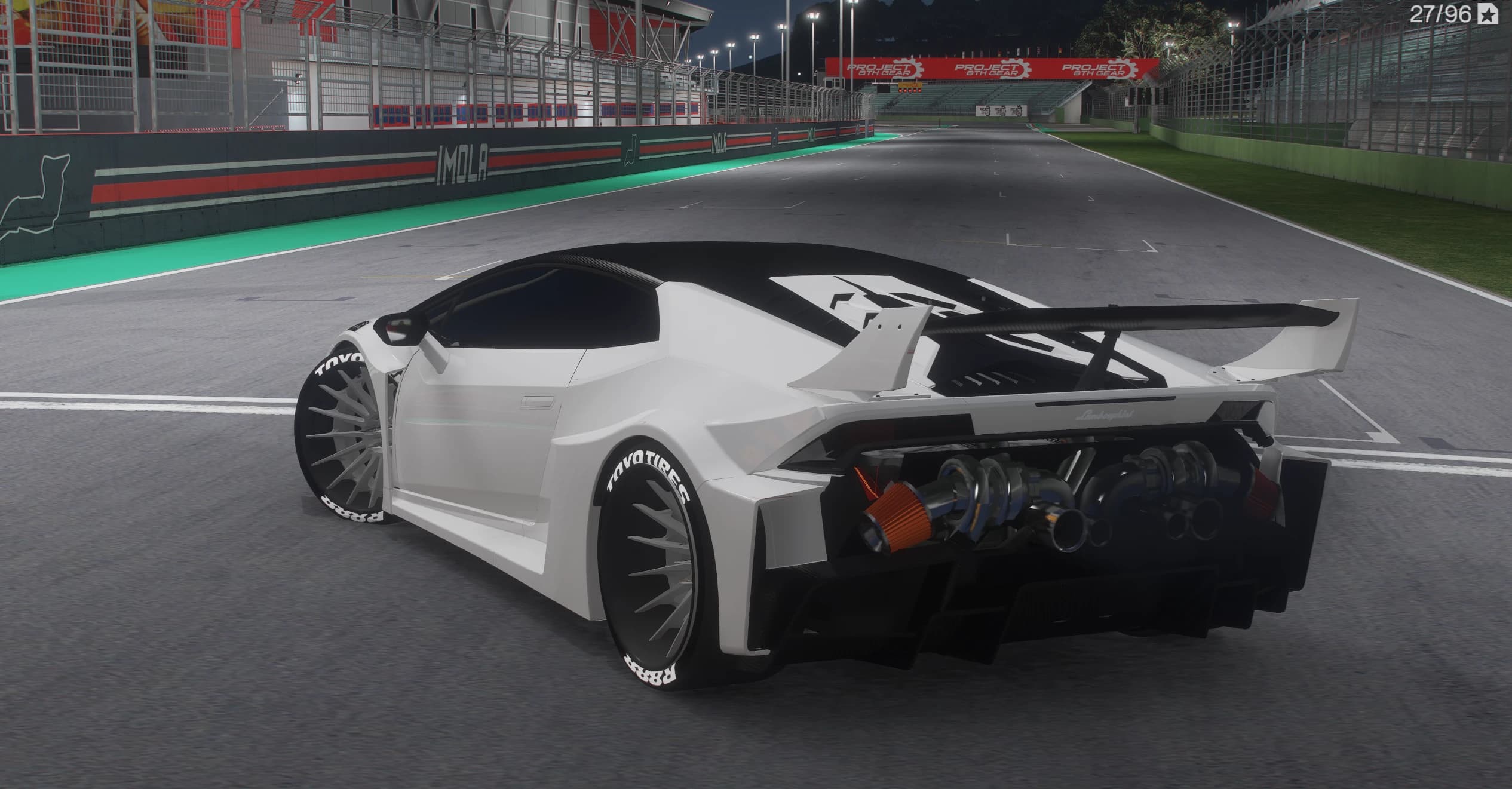 Tres cuartos trasero del Huracán blanco de noche en la recta de boxes, con el V10 al aire y sus admisiones a la vista tras la cabina, el alerón grande y los neumáticos anchos con letras Toyo