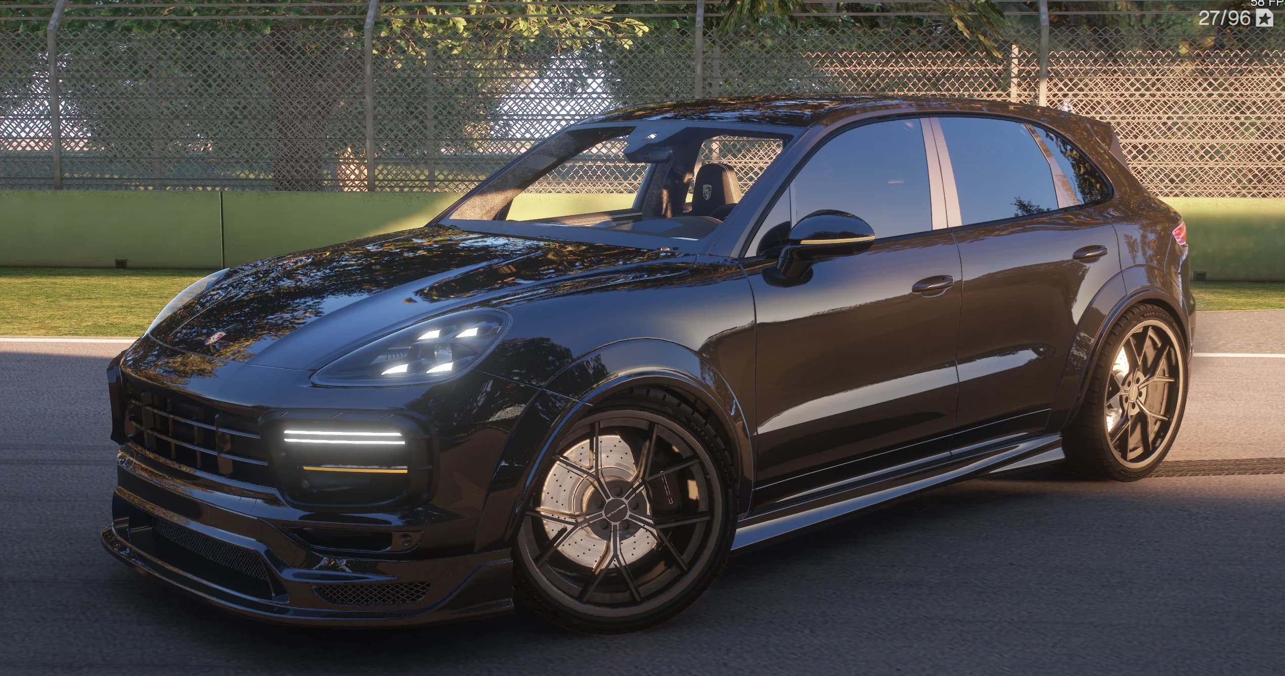 Porsche Cayenne en negro brillante con el kit Wald Black Bison, vista frontal en tres cuartos en un vial del circuito, con la barra de LED del paragolpes, los pasos de rueda ensanchados y el interior asomando por la ventanilla del conductor con el escudo Porsche en el reposacabezas
