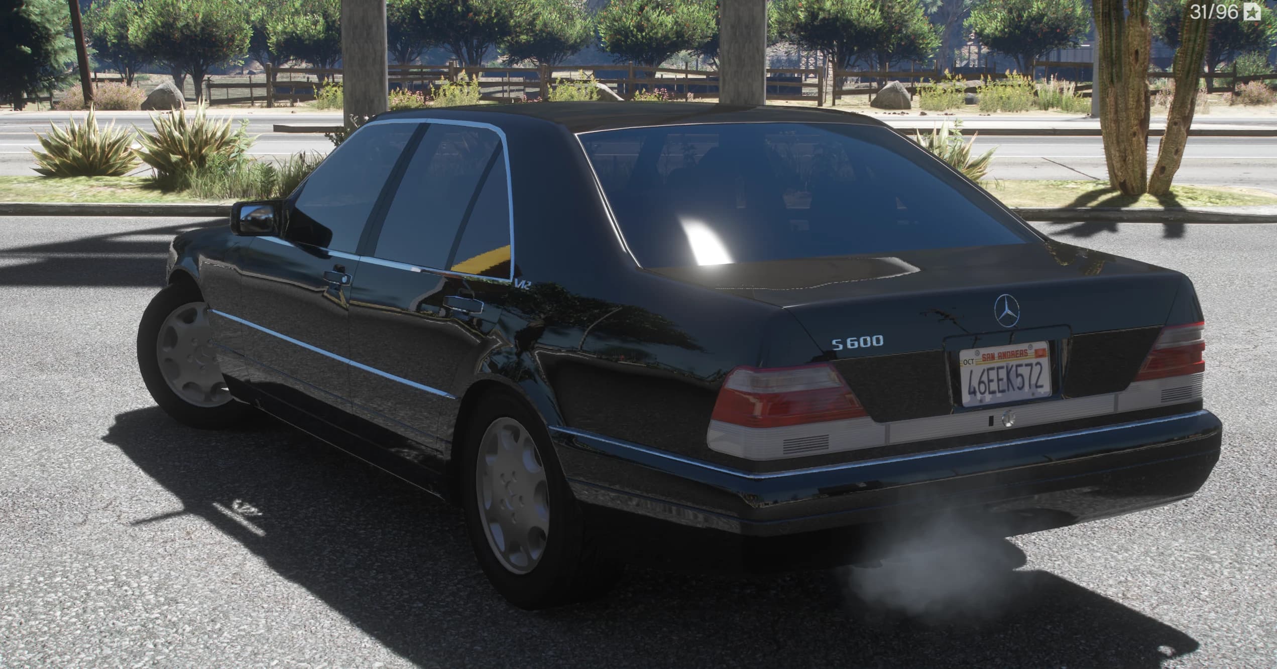 Vista trasera en tres cuartos con el anagrama S600 del maletero, el emblema V12 en el pilar y humo del escape, con una valla de madera de campo detrás