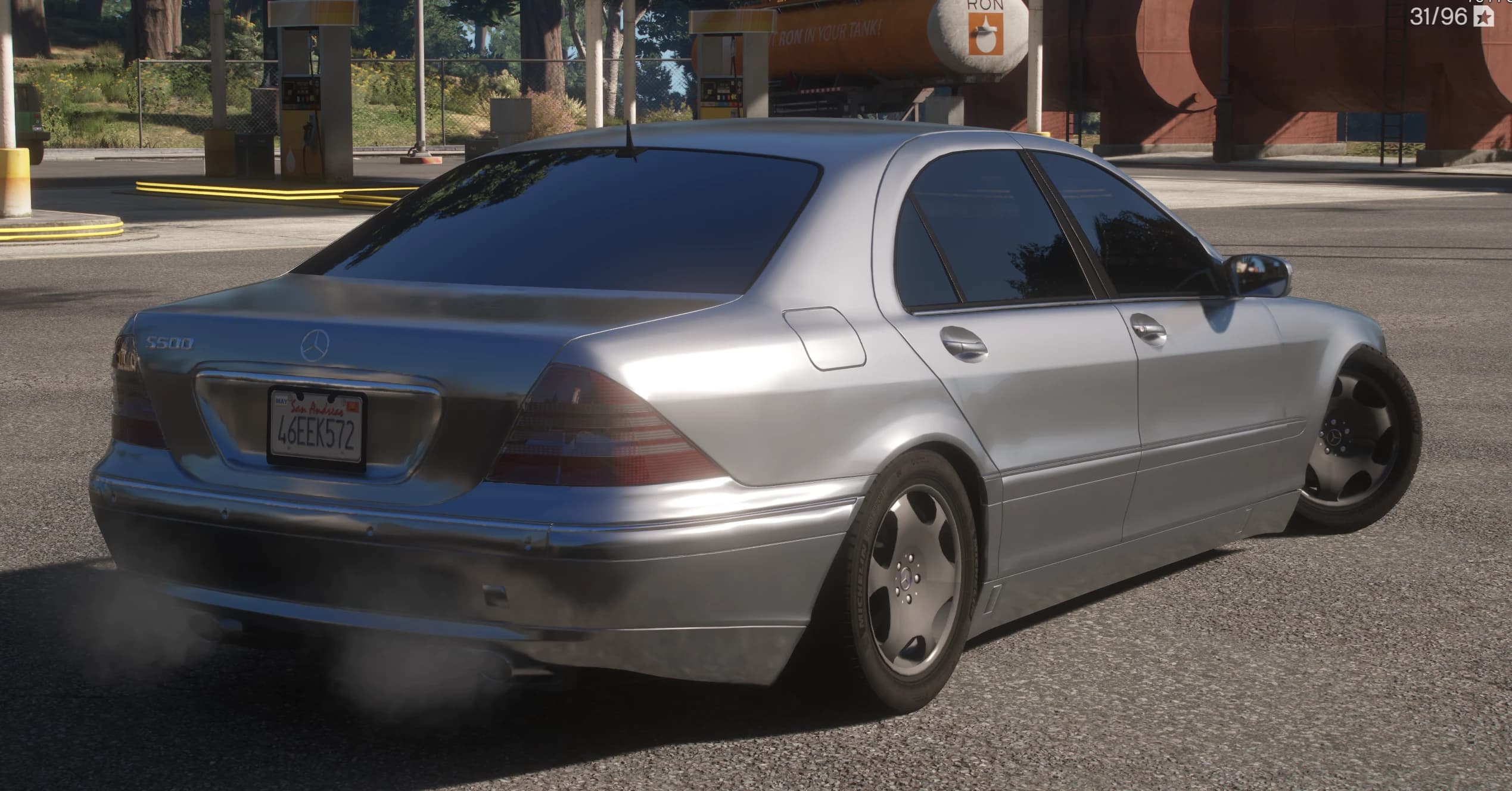 Vista trasera en tres cuartos en una gasolinera con el anagrama S500 del maletero, la matrícula de San Andreas, las letras Michelin en los neumáticos y un humo ligero del escape
