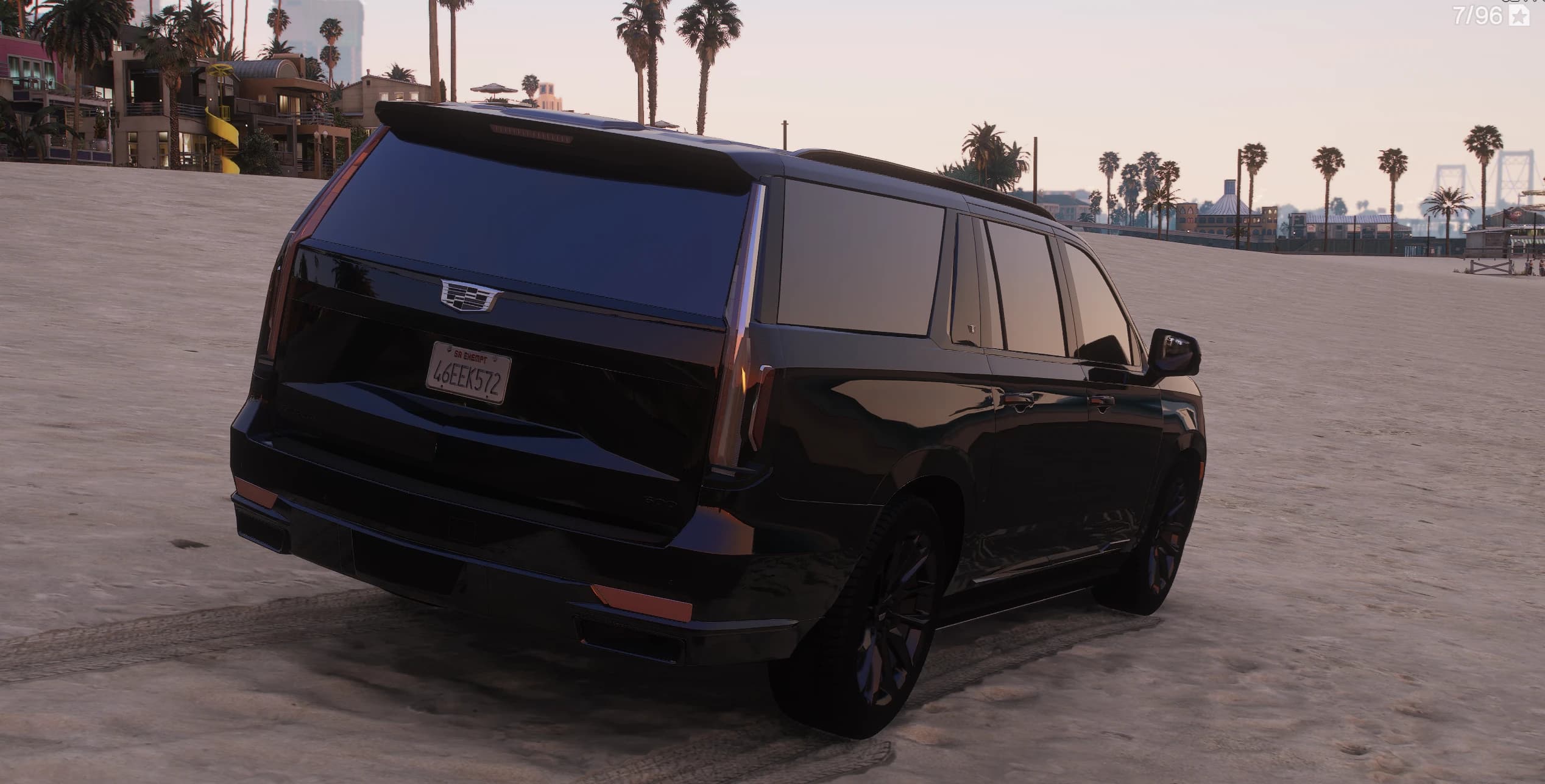 Tres cuartos trasero del Escalade negro en la playa, con el alerón de techo, el escudo de Cadillac en el portón y la matrícula de San Andreas 46EEK572, con palmeras y el muelle al fondo