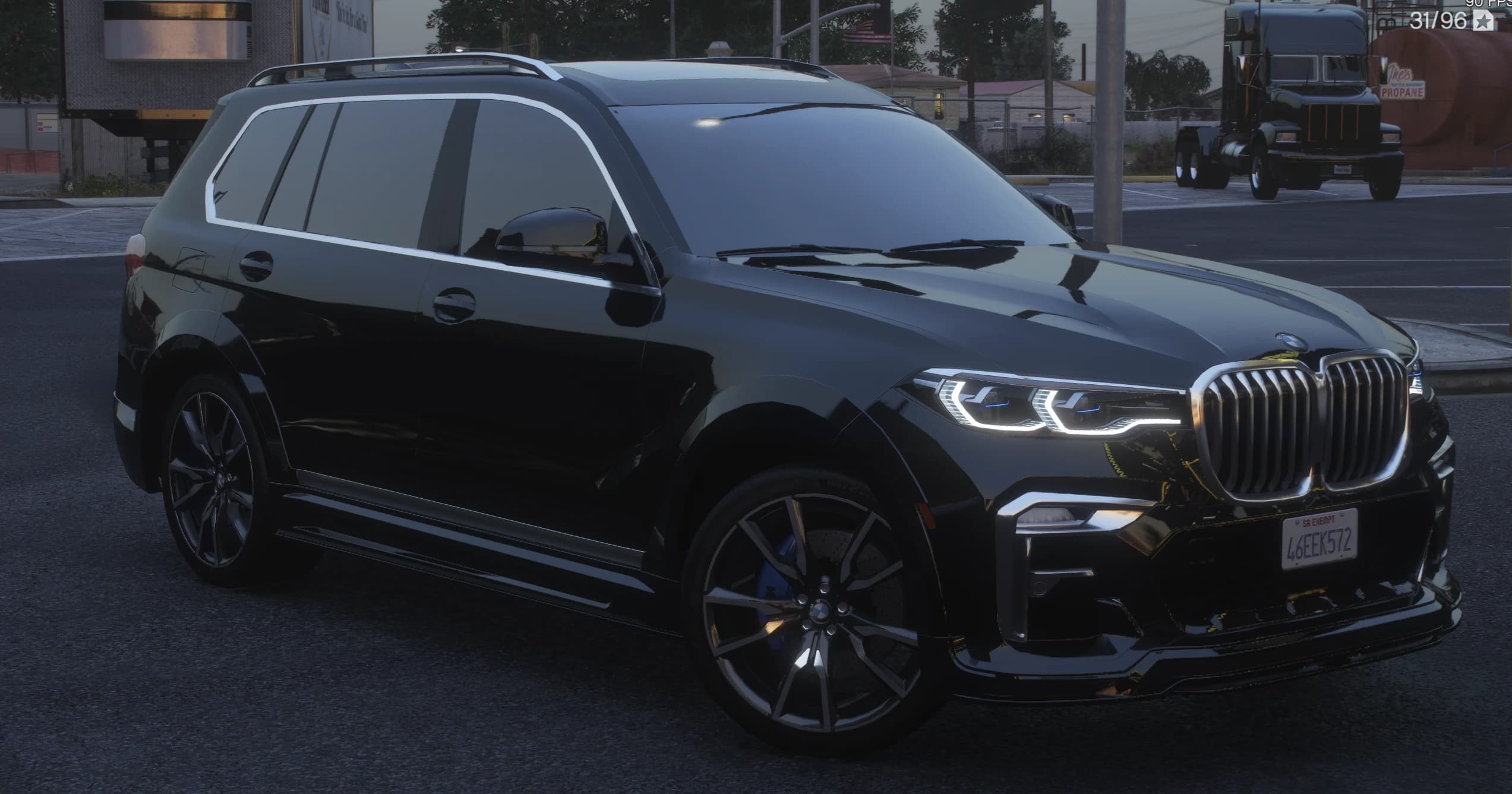 Vista frontal en tres cuartos del X7 negro al anochecer con la gran parrilla iluminada, faros LED encendidos y pinzas azules M tras llantas multirradio
