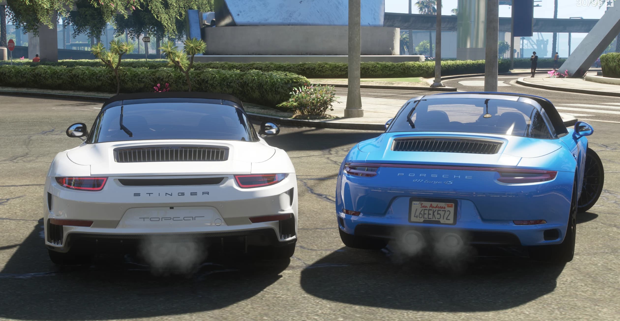 Vista trasera de ambos coches con los escapes humeando: el Topcar Stinger blanco con los rótulos STINGER y Topcar a la izquierda, y el 911 Targa 4S azul con la inscripción PORSCHE 911 targa 4S y una matrícula 46EEK572 a la derecha
