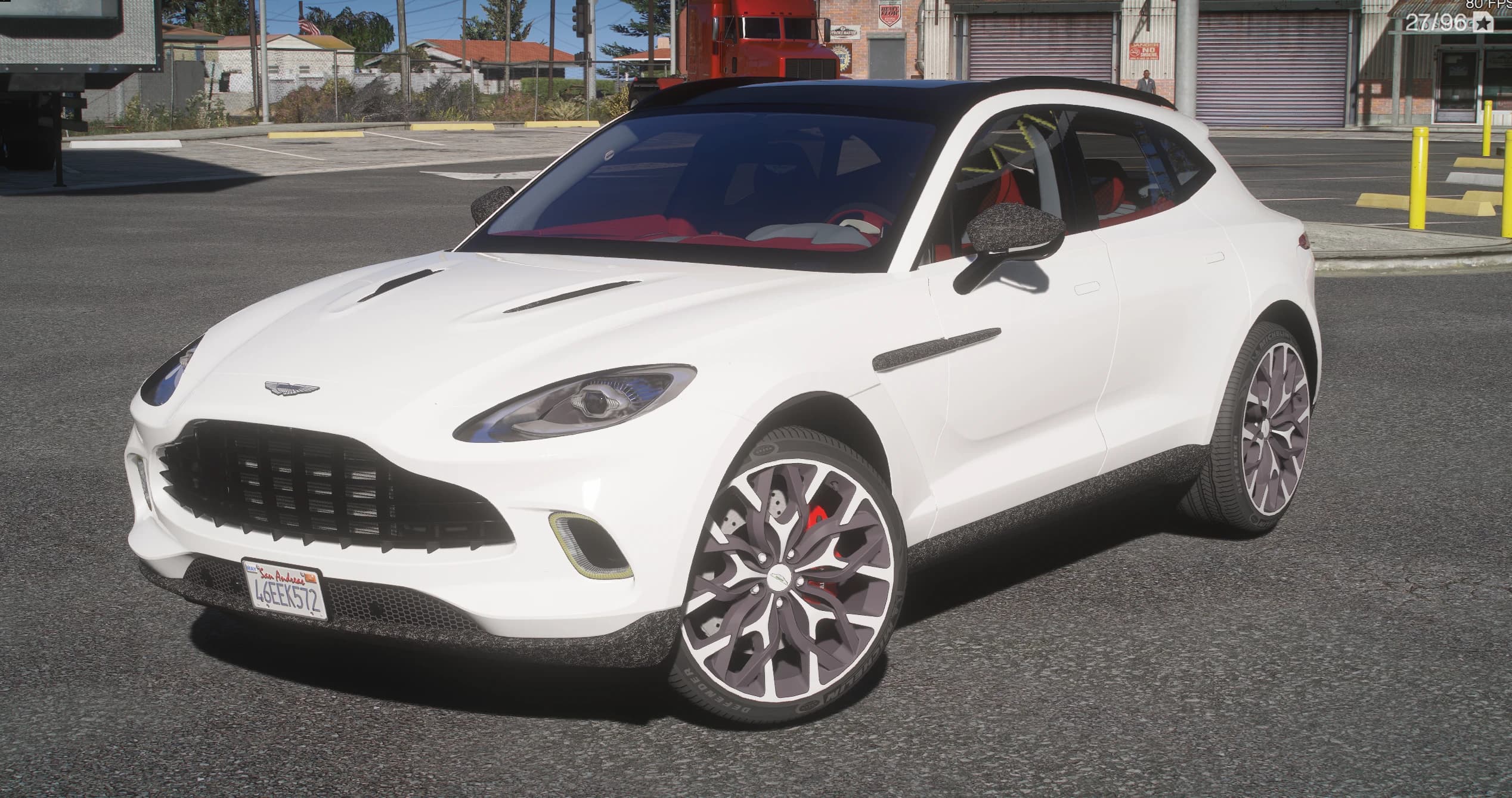 Aston Martin DBX Carbon Edition 2025 en blanco en una nave industrial, vista frontal en tres cuartos con el techo negro, las carcasas de los retrovisores y las branquias laterales en aspecto carbono, llantas multirradio grises y pinzas de freno rojas