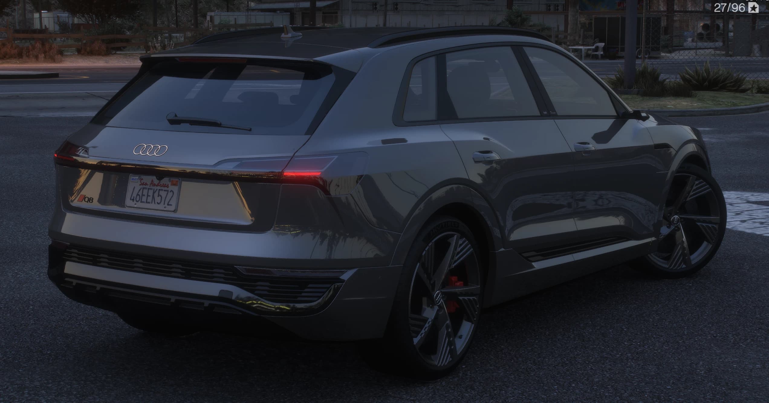 Tres cuartos trasero del Q8 E-Tron gris con el alerón de techo, los cuatro aros y el rótulo Q8 en rojo sobre el portón, la banda de luz trasera encendida y una matrícula de San Andreas