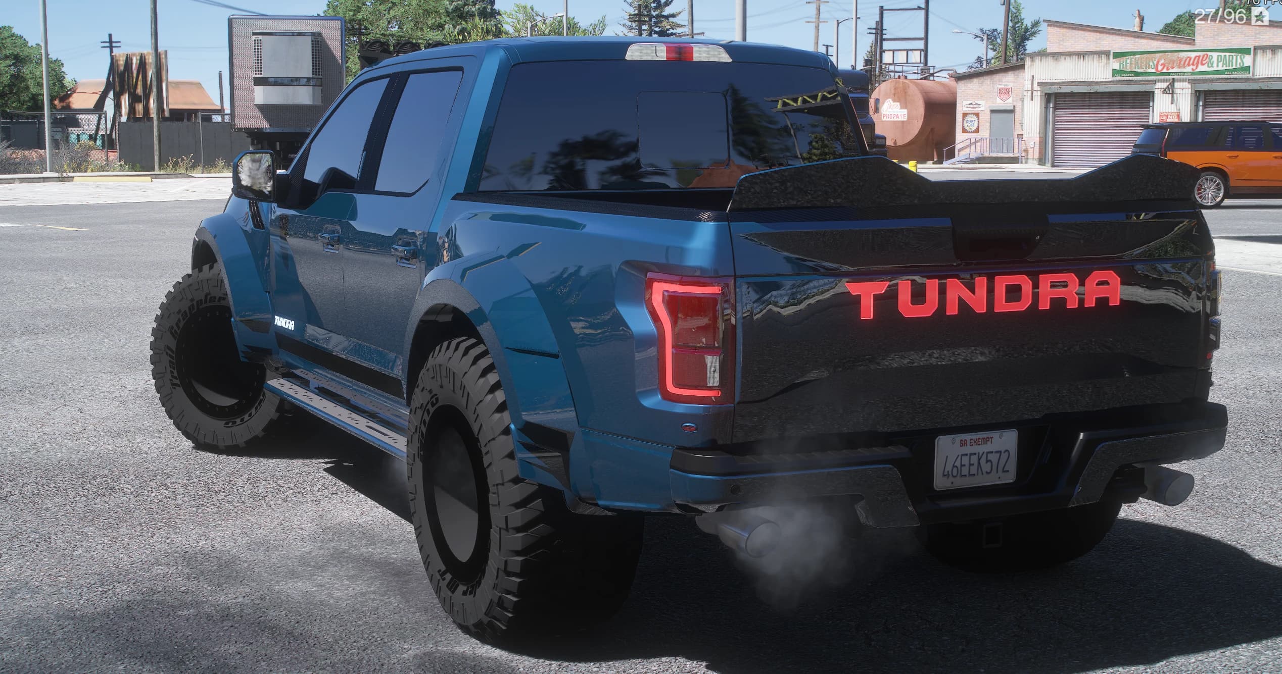 Tres cuartos trasero de la Tundra azul frente a un taller, con el rótulo TUNDRA iluminado en rojo cruzando el portón, la tapa negra de la caja, los estribos laterales y humo del escape