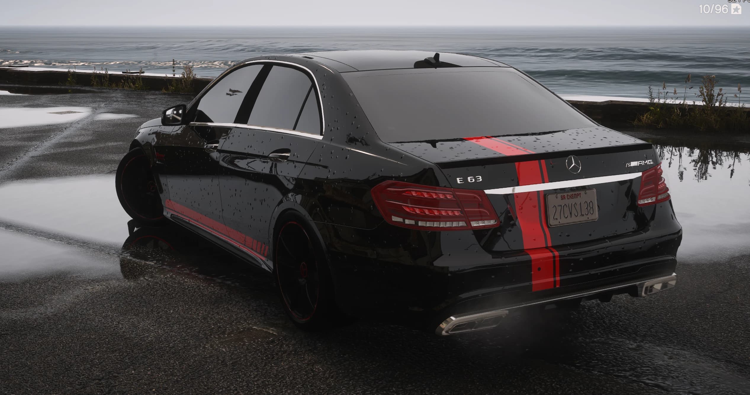 Tres cuartos trasero del E63 S AMG negro con los emblemas E 63 y S AMG, la franja roja y el escape cuádruple junto al mar