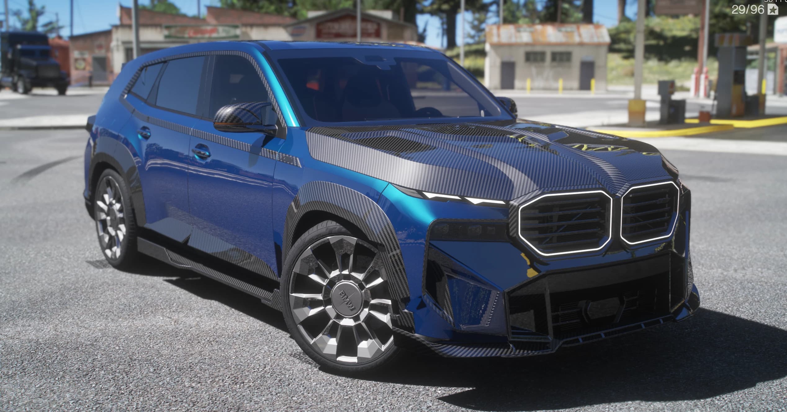SUV BMW XM G09 azul con paneles de carbono y la parrilla de doble riñón iluminada, tres cuartos frontal en una gasolinera