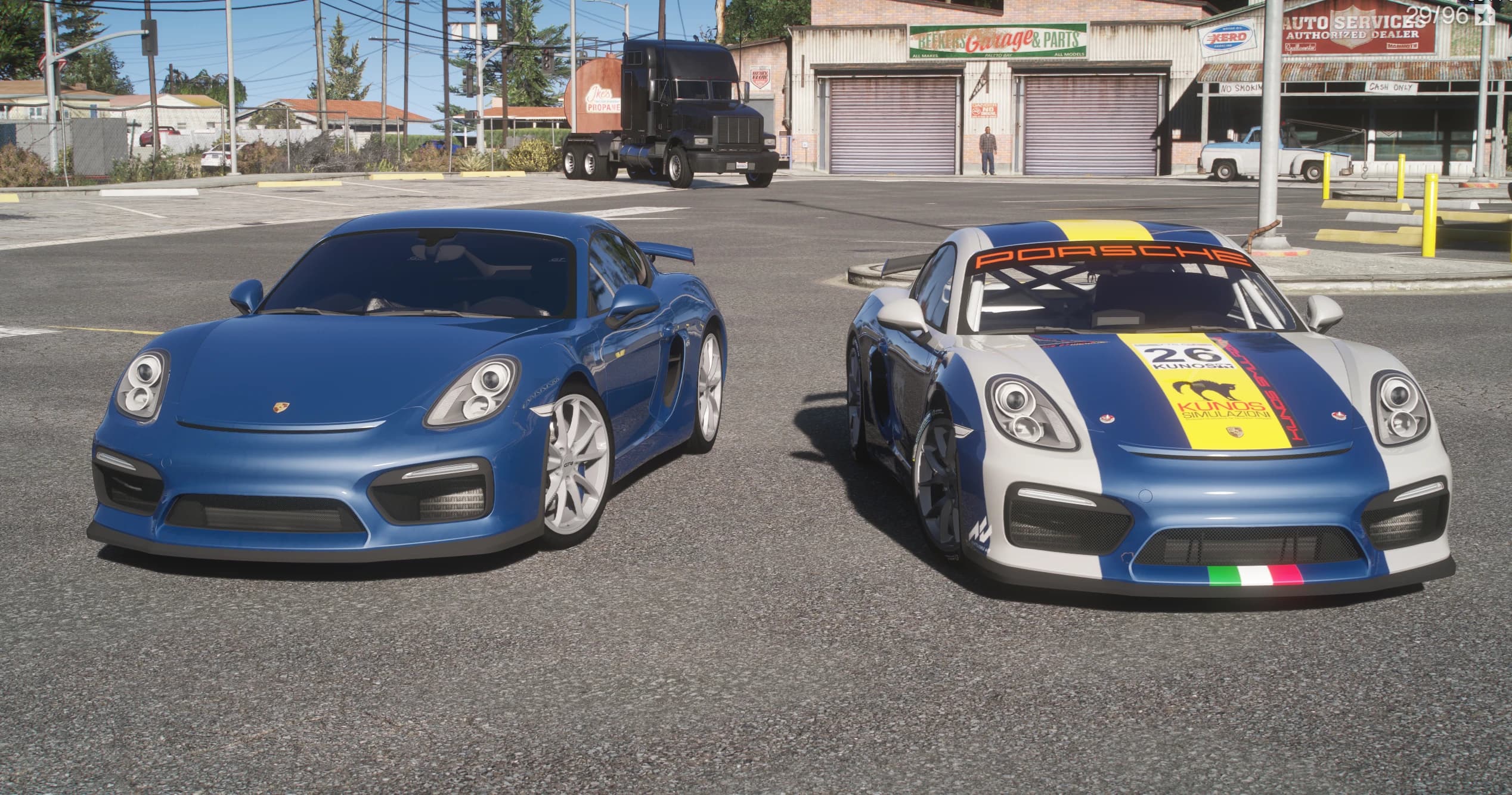 Porsche Cayman GT4 de calle en azul a la izquierda junto al GT4 Clubsport de competición en blanco y azul, con el número 26 y una franja amarilla, frente a un taller