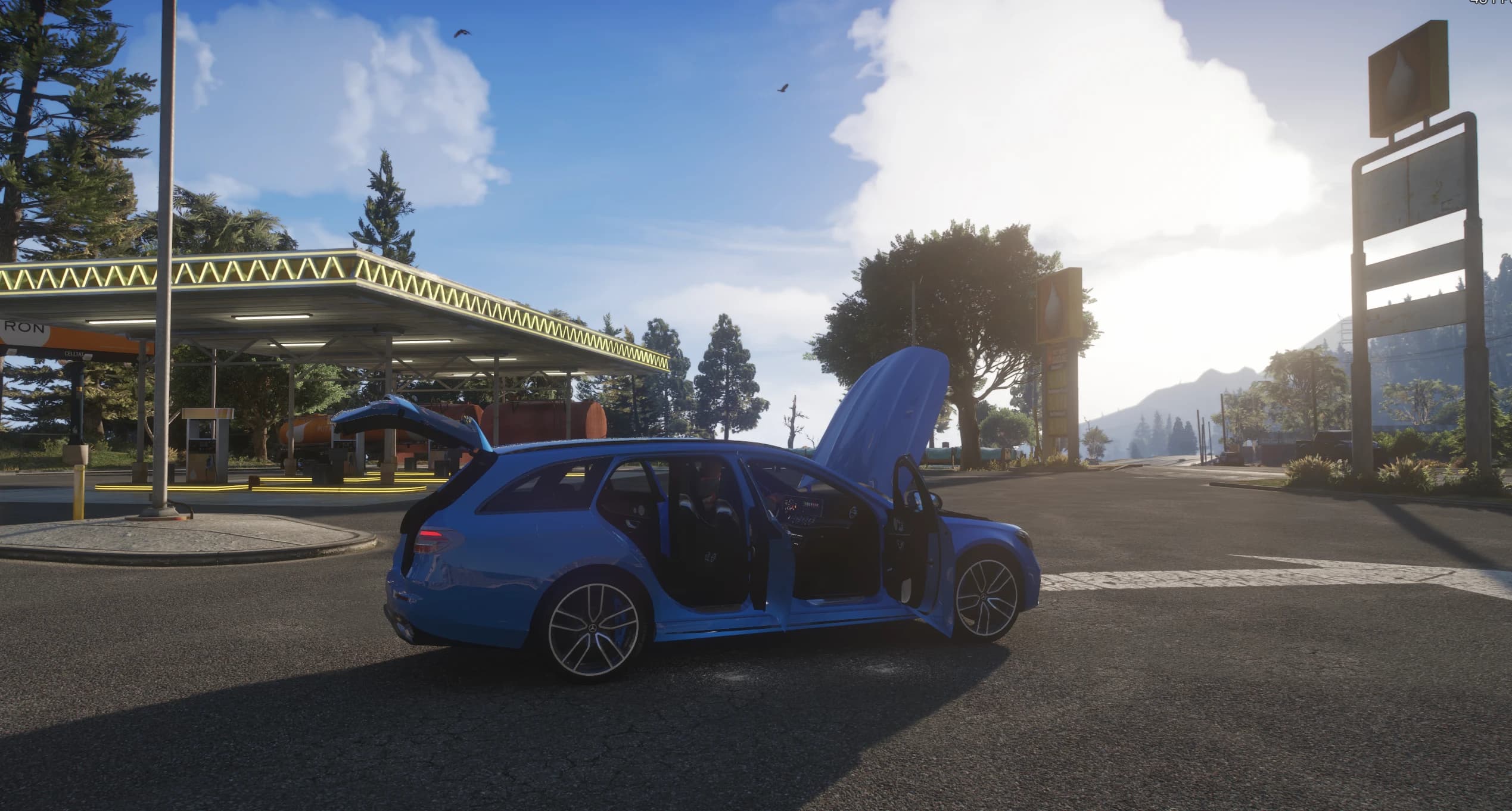 Una variante en azul del E63 S Estate con las puertas, el capó y el portón trasero abiertos en una gasolinera, mostrando el interior y el maletero