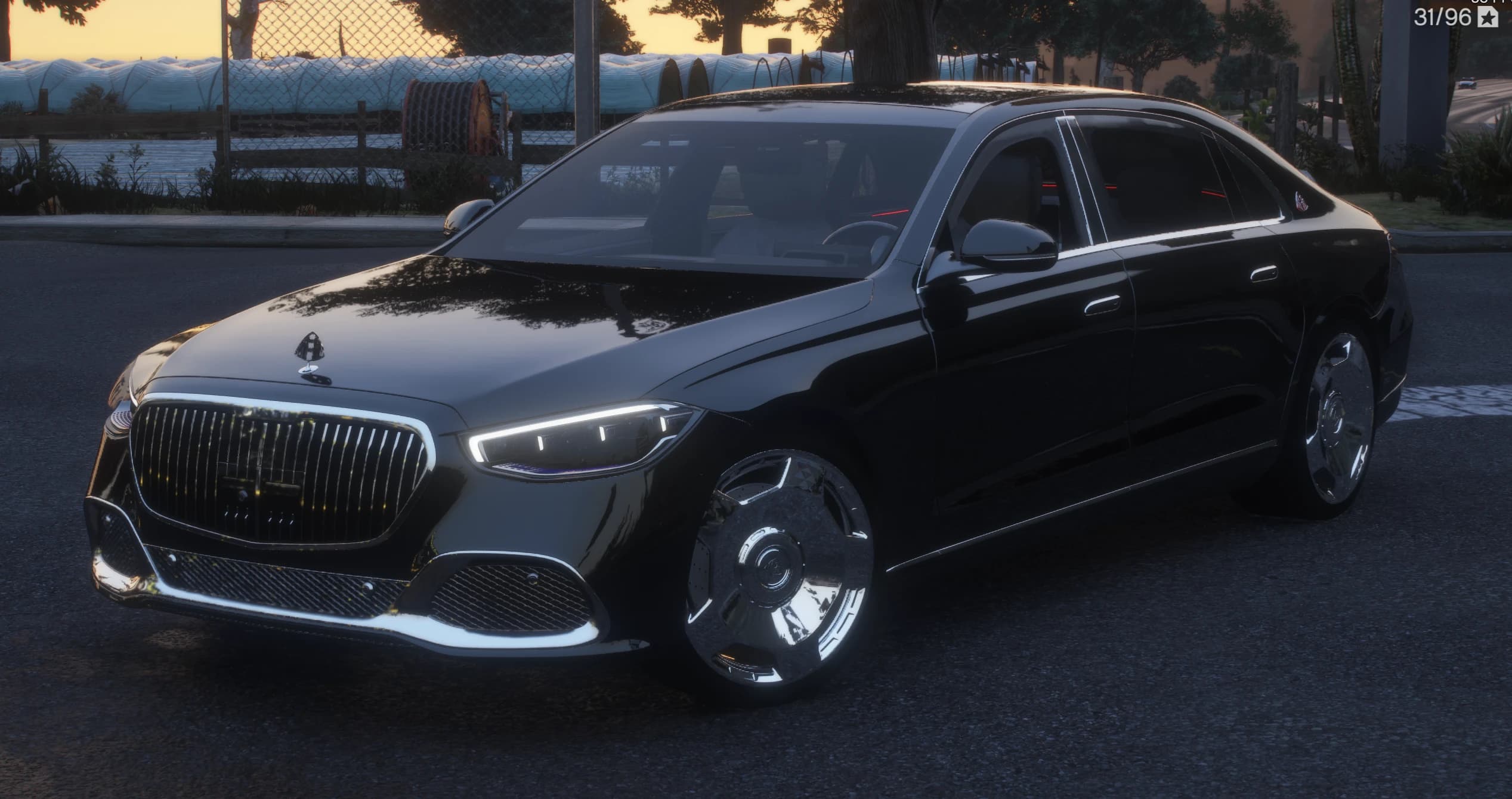 Vista frontal en tres cuartos del Maybach S580 negro al anochecer con la parrilla cromada de lamas verticales, la insignia del capó y llantas pulidas de plato, junto a una valla de granja