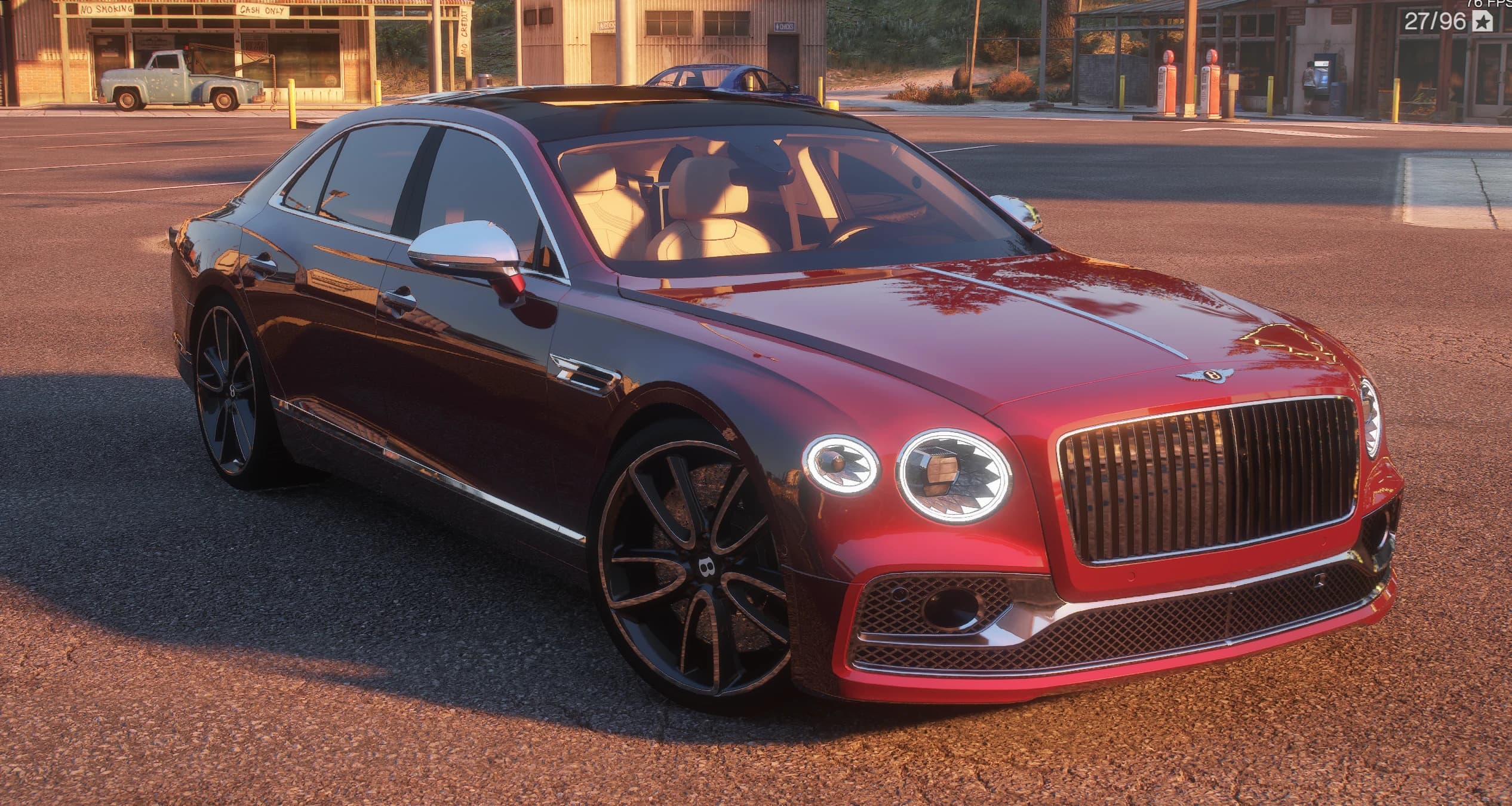 Bentley Flying Spur W12 2024 en rojo cereza con techo negro, tres cuartos delantero con el sol bajo, parrilla cromada de malla con la B alada, faros redondos tallados y llantas negras multirradio