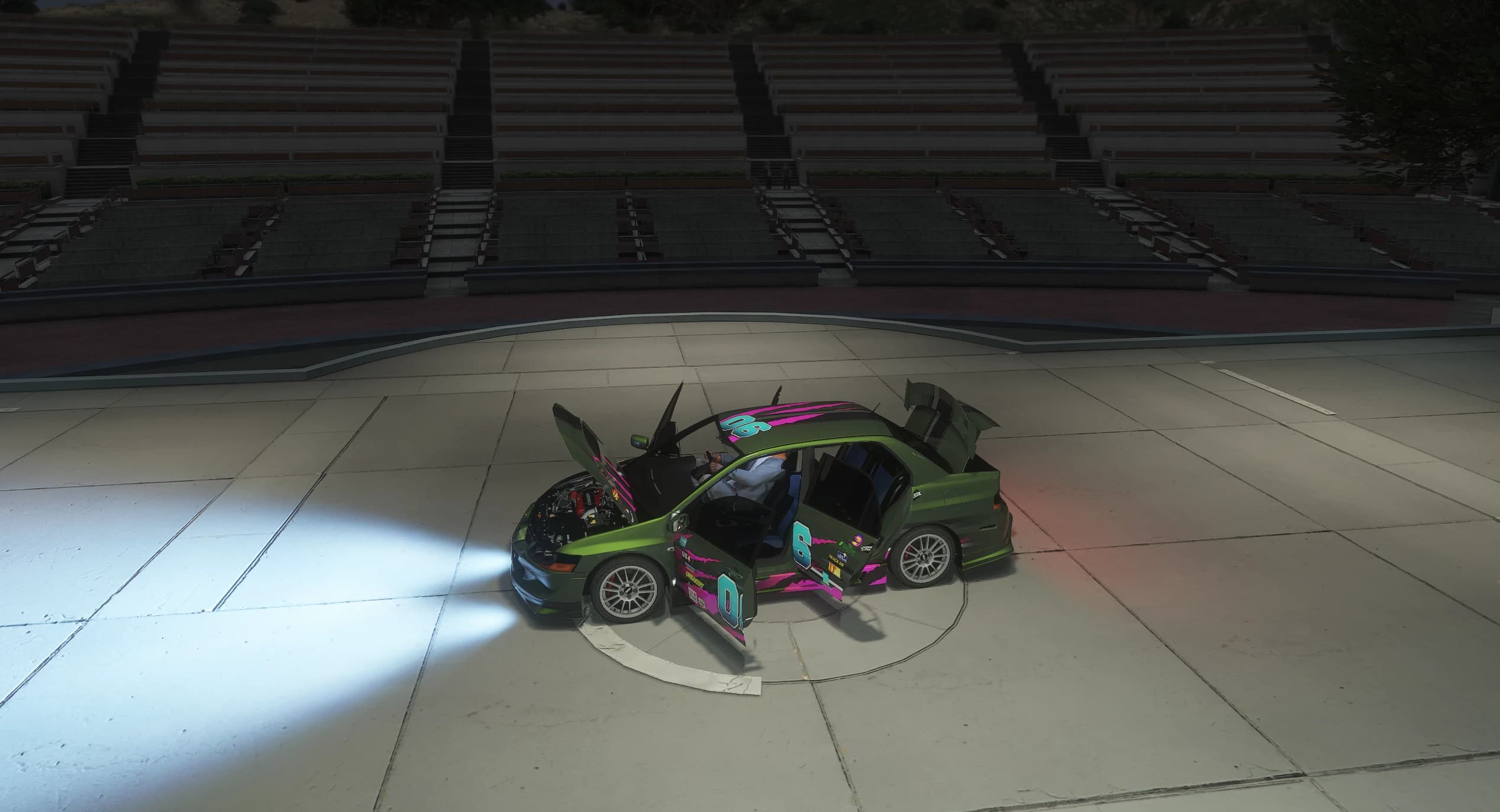 Plano cenital nocturno en el anfiteatro de Vinewood con el capó, las dos puertas izquierdas y el maletero abiertos, el conductor sentado dentro y los faros encendidos