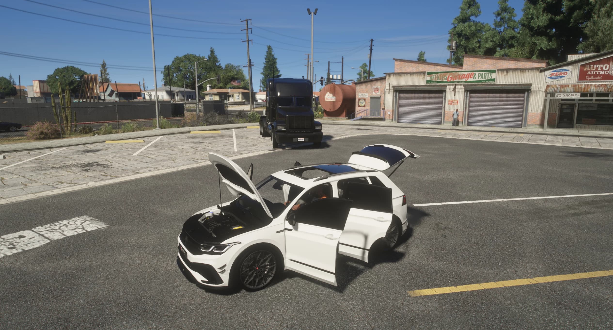 El Tiguan en un aparcamiento con el capó, las puertas y el portón abiertos, enseñando el vano motor y el techo panorámico de cristal, con un taller y un camión negro detrás