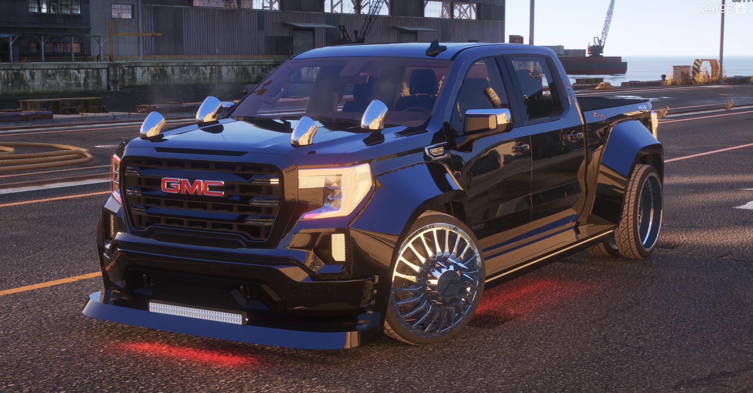 El GMC Sierra negro en un astillero con luces tipo bala en el techo, llantas dually cromadas y luz inferior roja