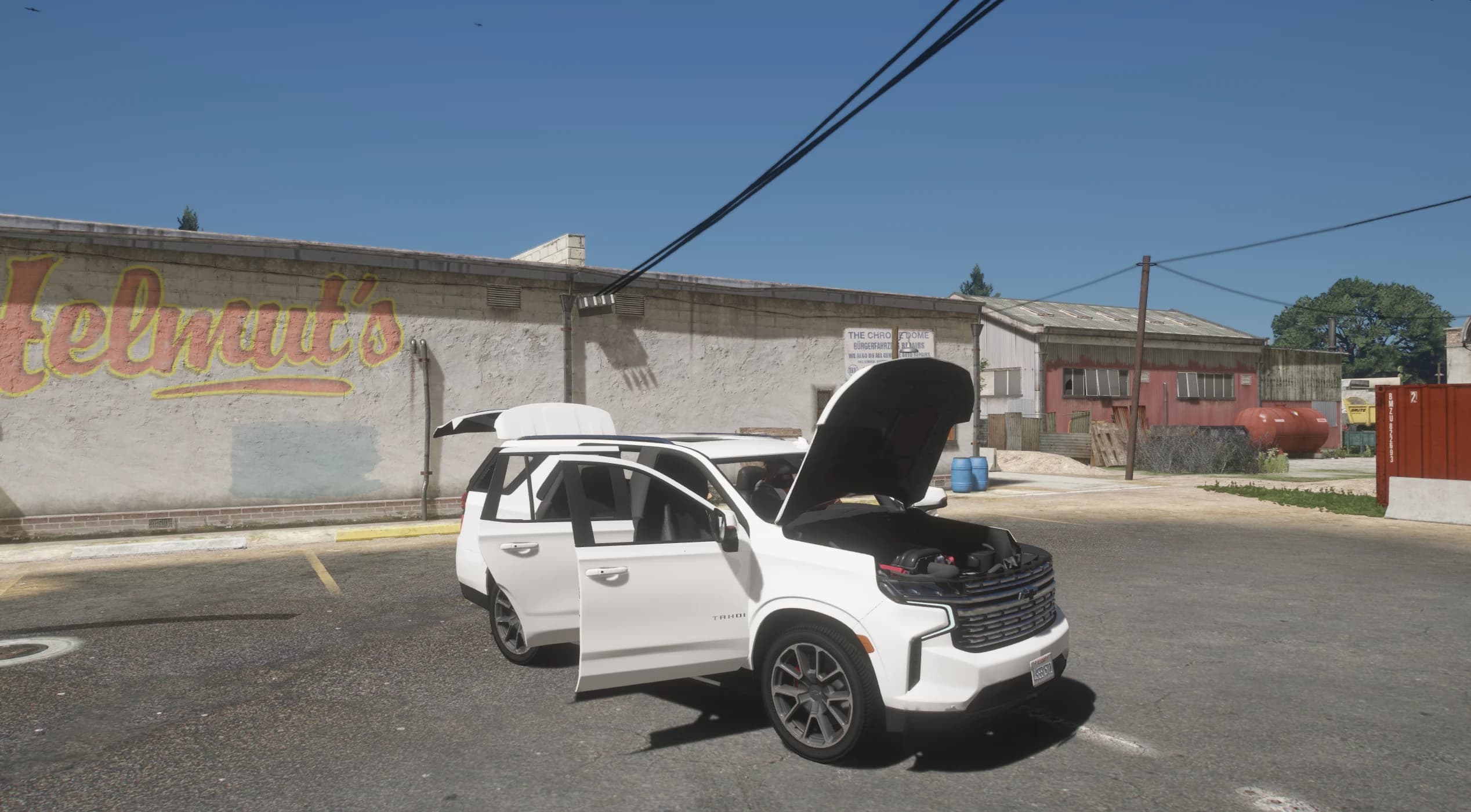 El Tahoe aparcado junto a un muro con el mural de Helmut's, con el capó, las puertas y el portón abiertos y el vano motor a la vista