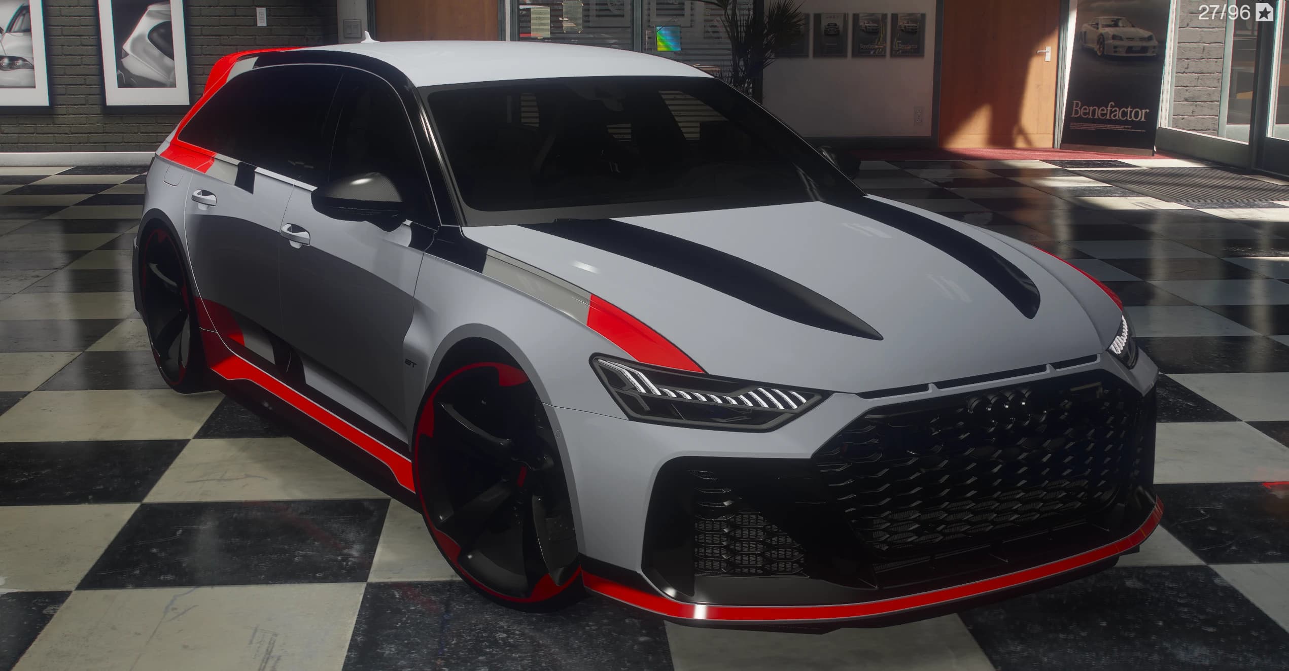 Audi RS6 GT 2025 familiar en gris nardo con grafismos GT en rojo y negro, tres cuartos delantero sobre el suelo ajedrezado de un concesionario, parrilla de panal negra y llantas negras con el borde rojo