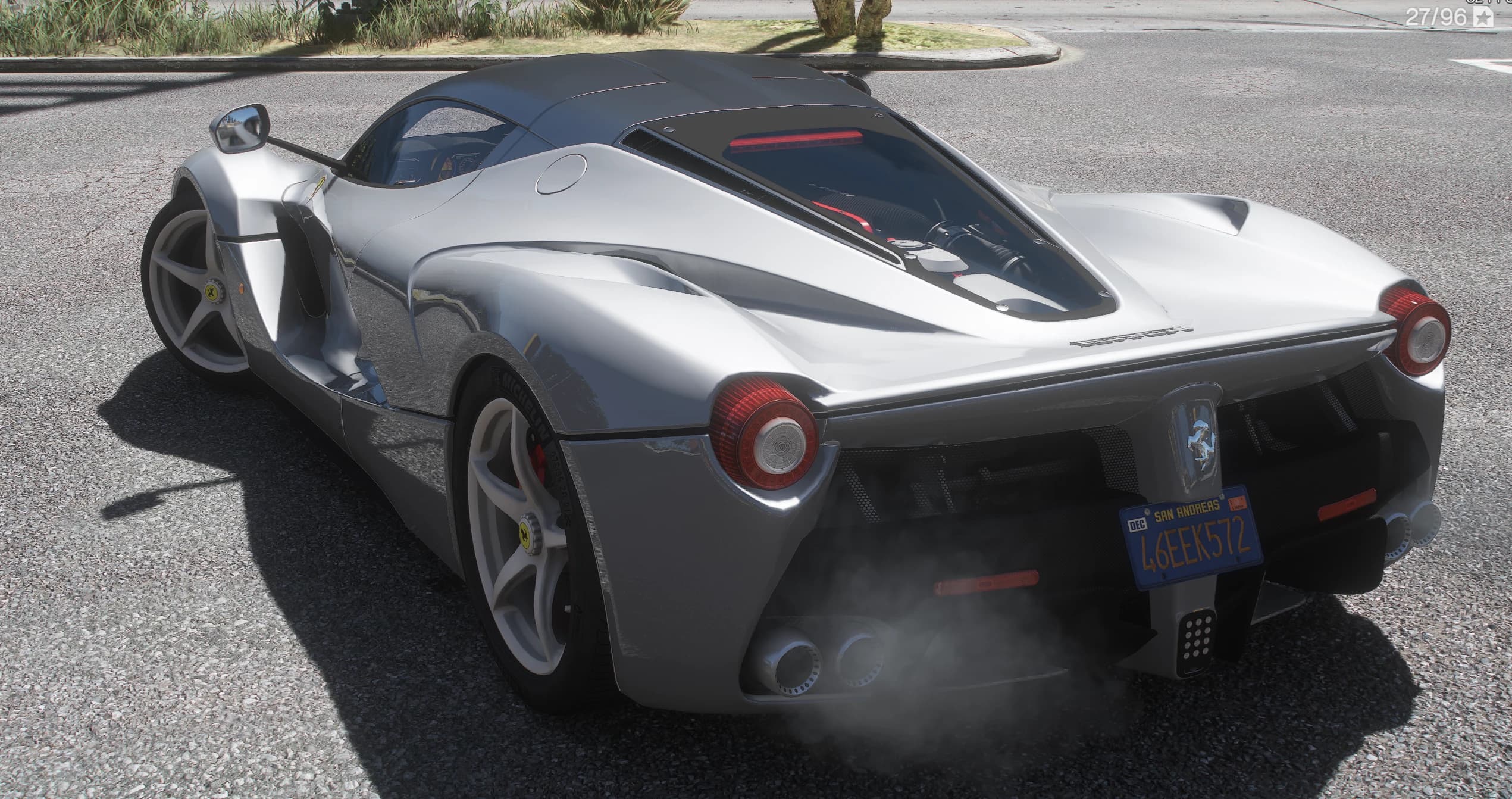 Tres cuartos trasero del LaFerrari plateado con el V12 bajo la tapa de motor acristalada, los pilotos redondos, el escudo del cavallino y humo saliendo de los dos escapes