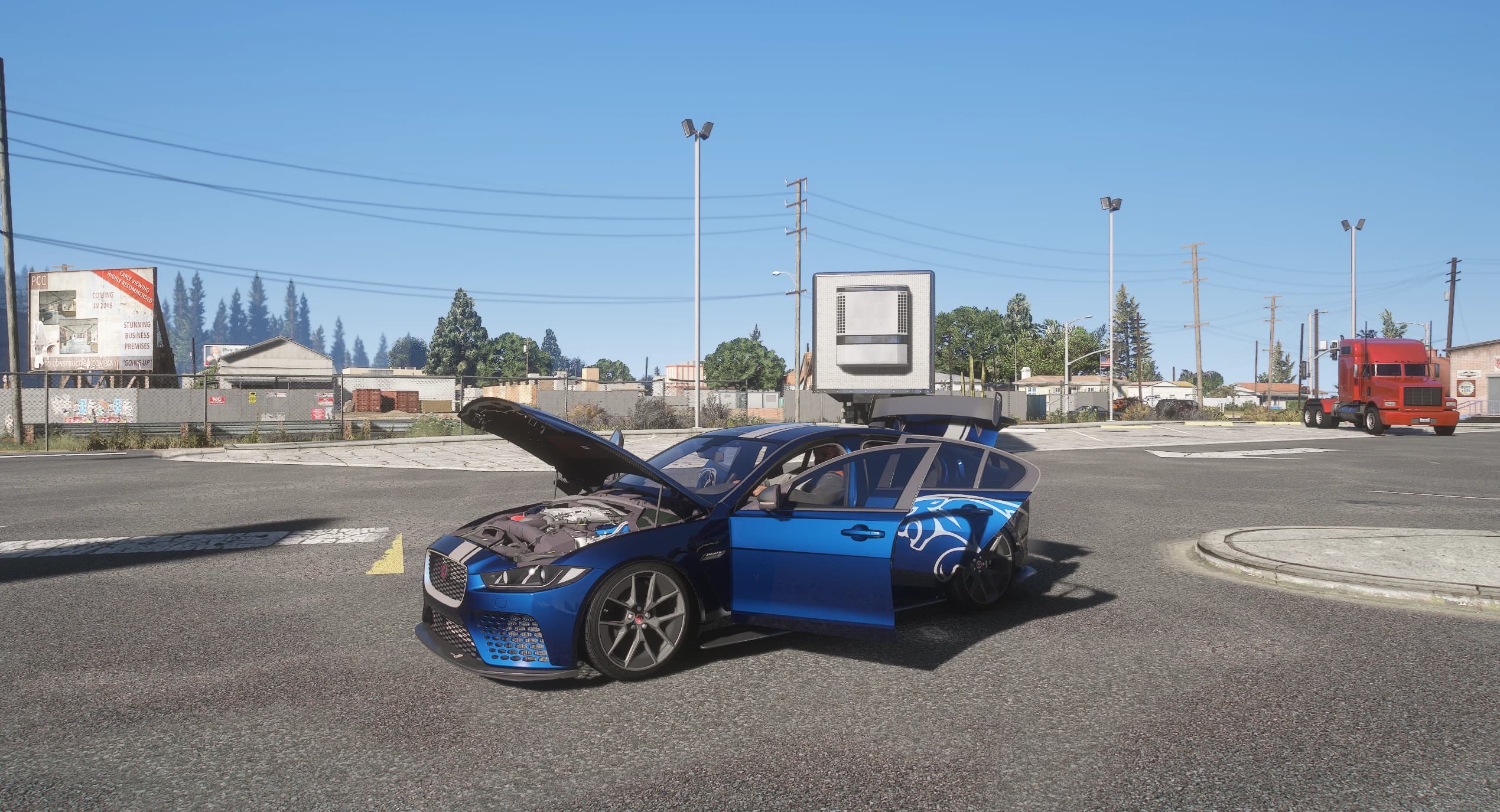 El Project 8 parado en un cruce ancho con el capó y las dos puertas del lado izquierdo abiertos, dejando ver el vano motor y la cabina, con un camión rojo y naves industriales al fondo