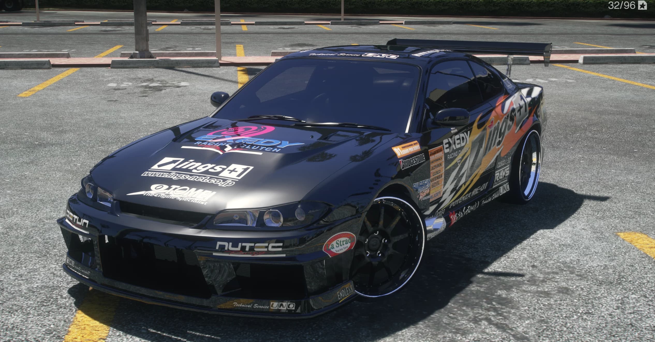Vista frontal en tres cuartos del Silvia S15 negro con el livery de llamas ings+1, el logo EXEDY en el capó, la columna de patrocinadores en la puerta y un alerón GT alto