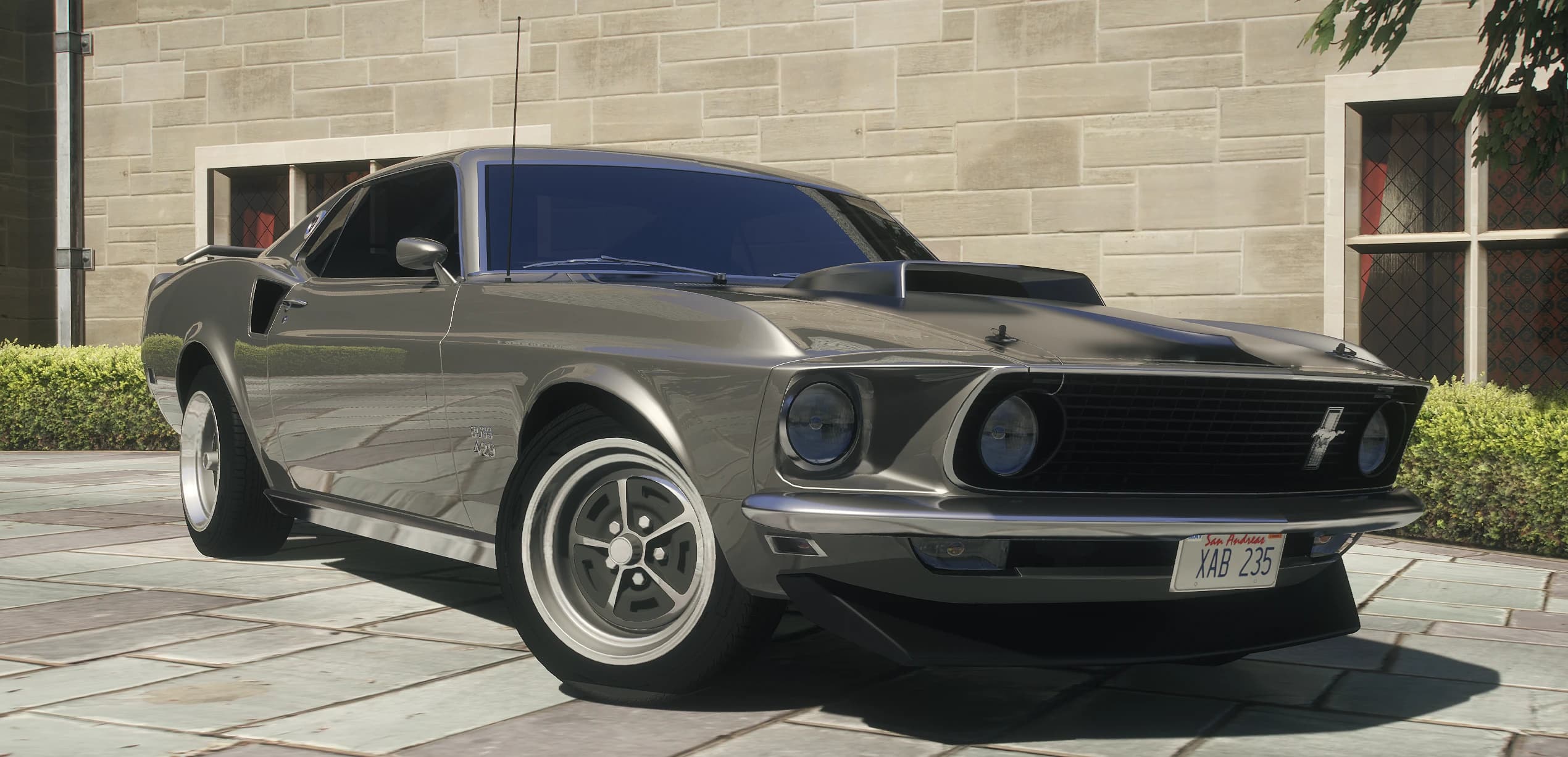 Vista frontal en tres cuartos del Mustang Boss 429 de 1969 gris plomo con la toma de aire del capó frente a una mansión de piedra
