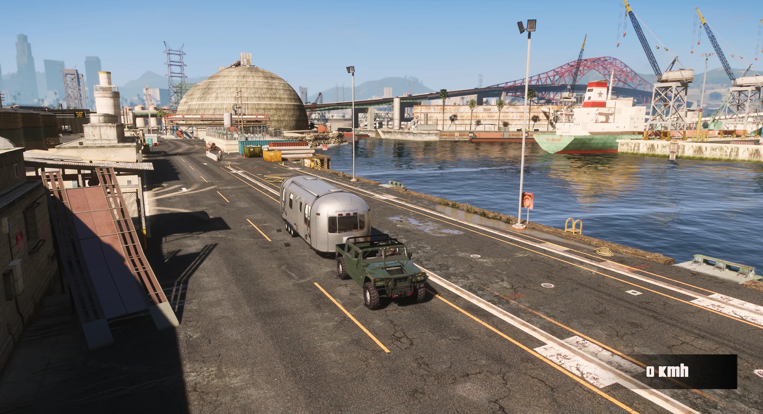 Vista elevada del puerto con el H1 Alpha Open Top verde junto a una caravana plateada, con grúas, un carguero amarrado y el puente del puerto al fondo