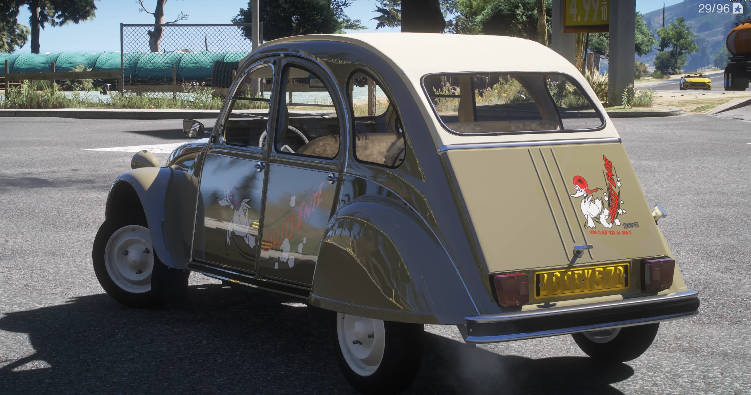 Trasera con el pato y el rótulo 2CV6 en el portón del maletero y matrícula amarilla trasera, en una gasolinera