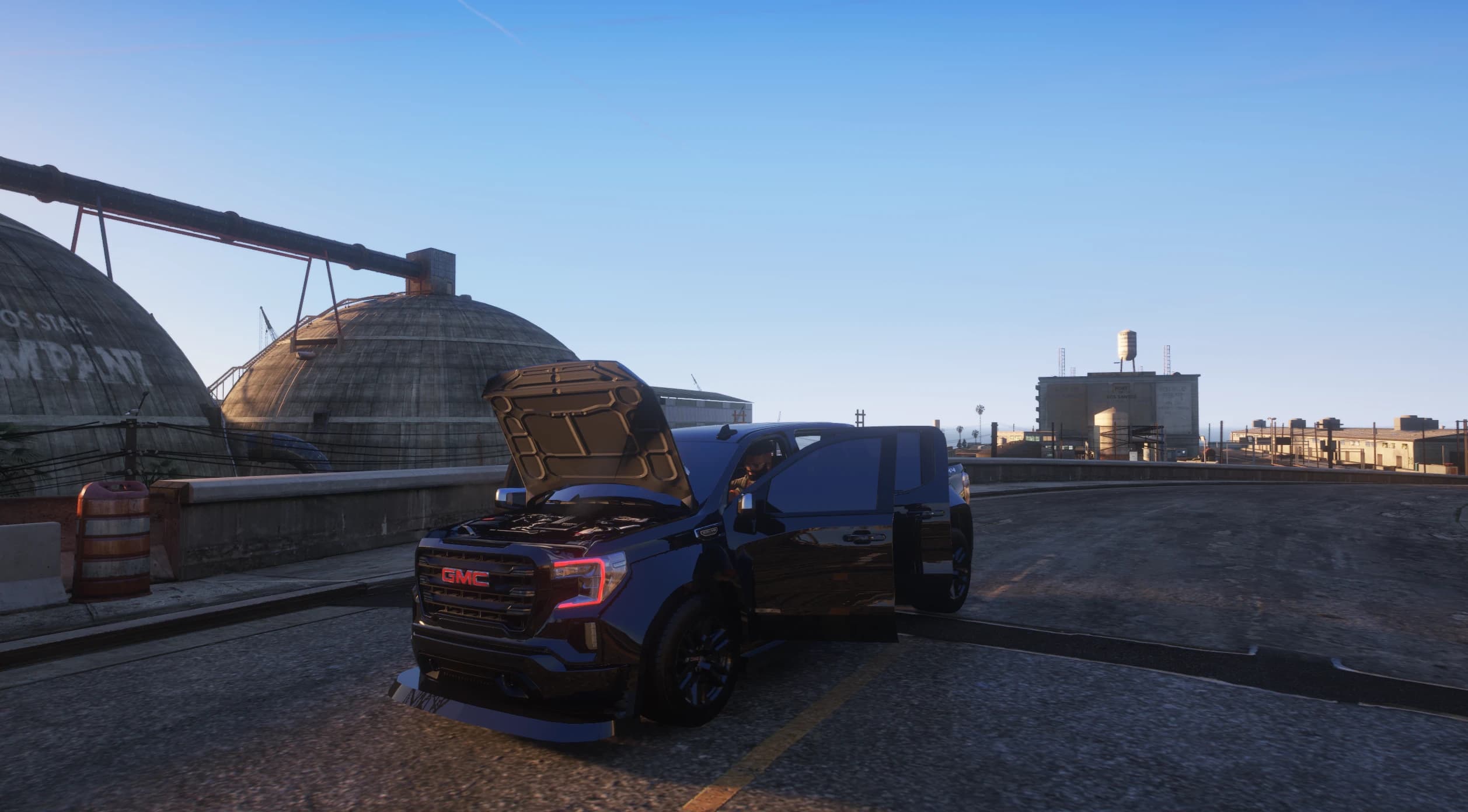 El GMC Sierra con el capó y la puerta del conductor abiertos junto a las cúpulas de la cementera, mostrando la bahía del motor modelada