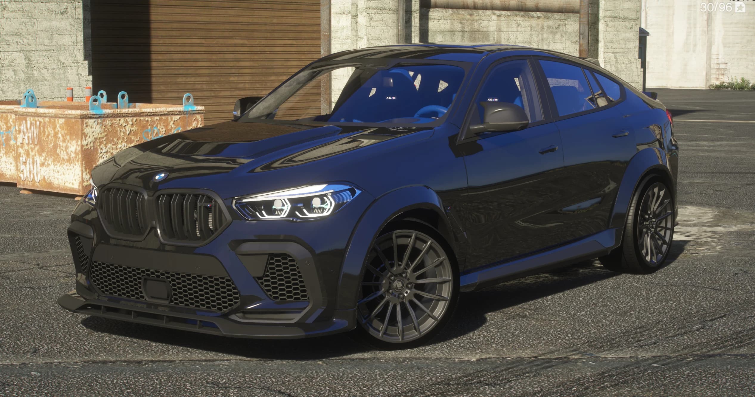 Tres cuartos frontal del BMW X6M 2023 azul oscuro con el kit widebody de Prior Design, con la parrilla riñón en negro y acento rojo M, el splitter delantero de carbono, los pasos de rueda ensanchados y el interior M azul con asientos X6 M