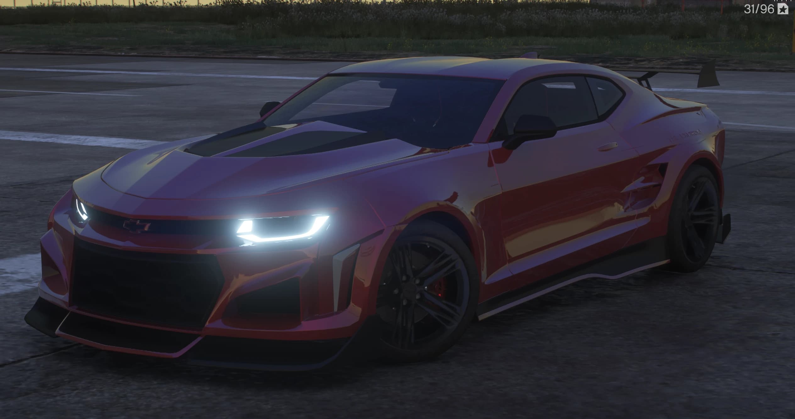Vista frontal en tres cuartos del Camaro ZL1 rojo al anochecer con los faros LED encendidos, inserto negro en el capó y splitter con canards