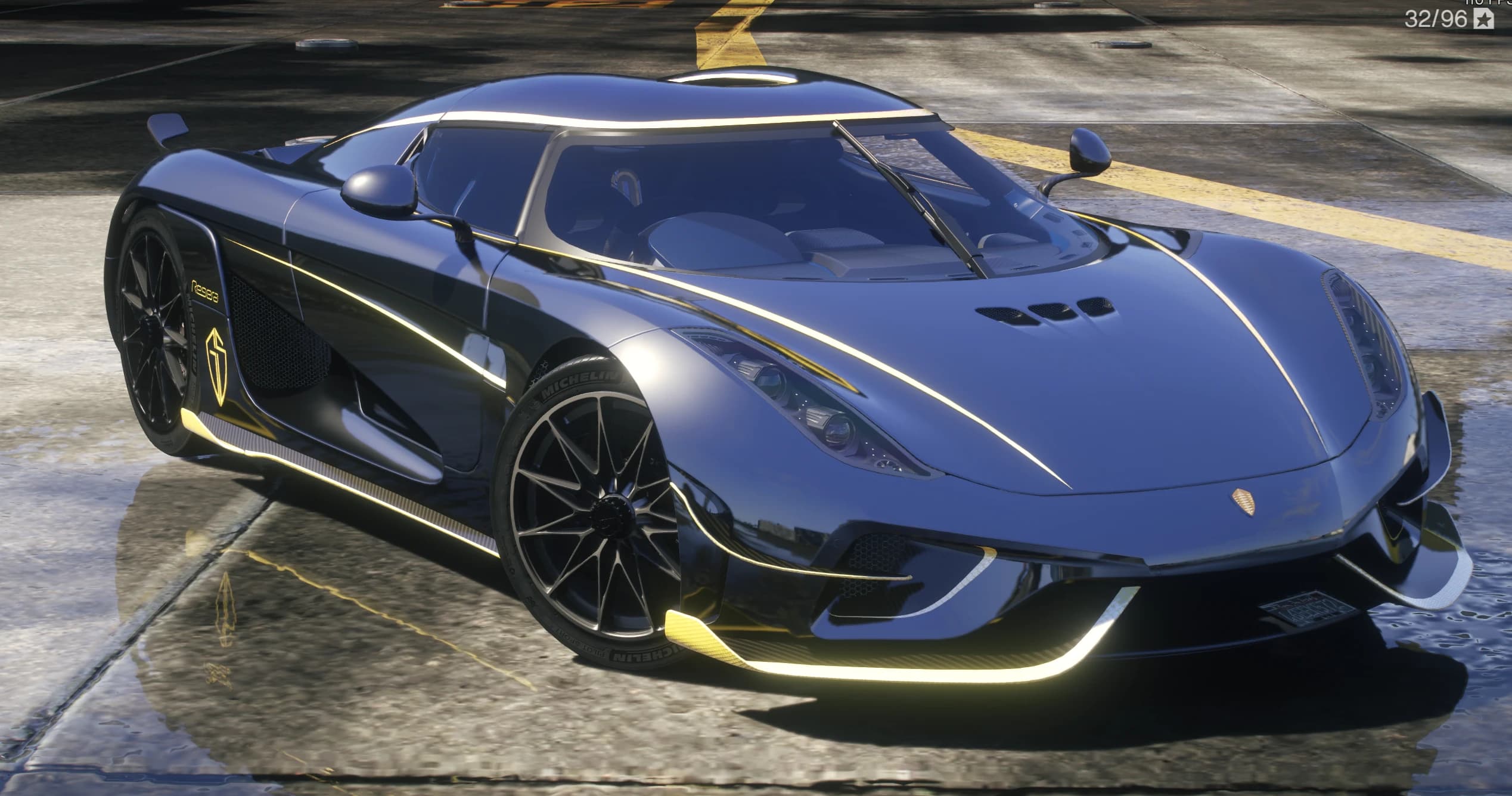 Vista frontal en tres cuartos del Regera azul oscuro con perfiles dorados, el escudo fantasma dorado y neumáticos Michelin