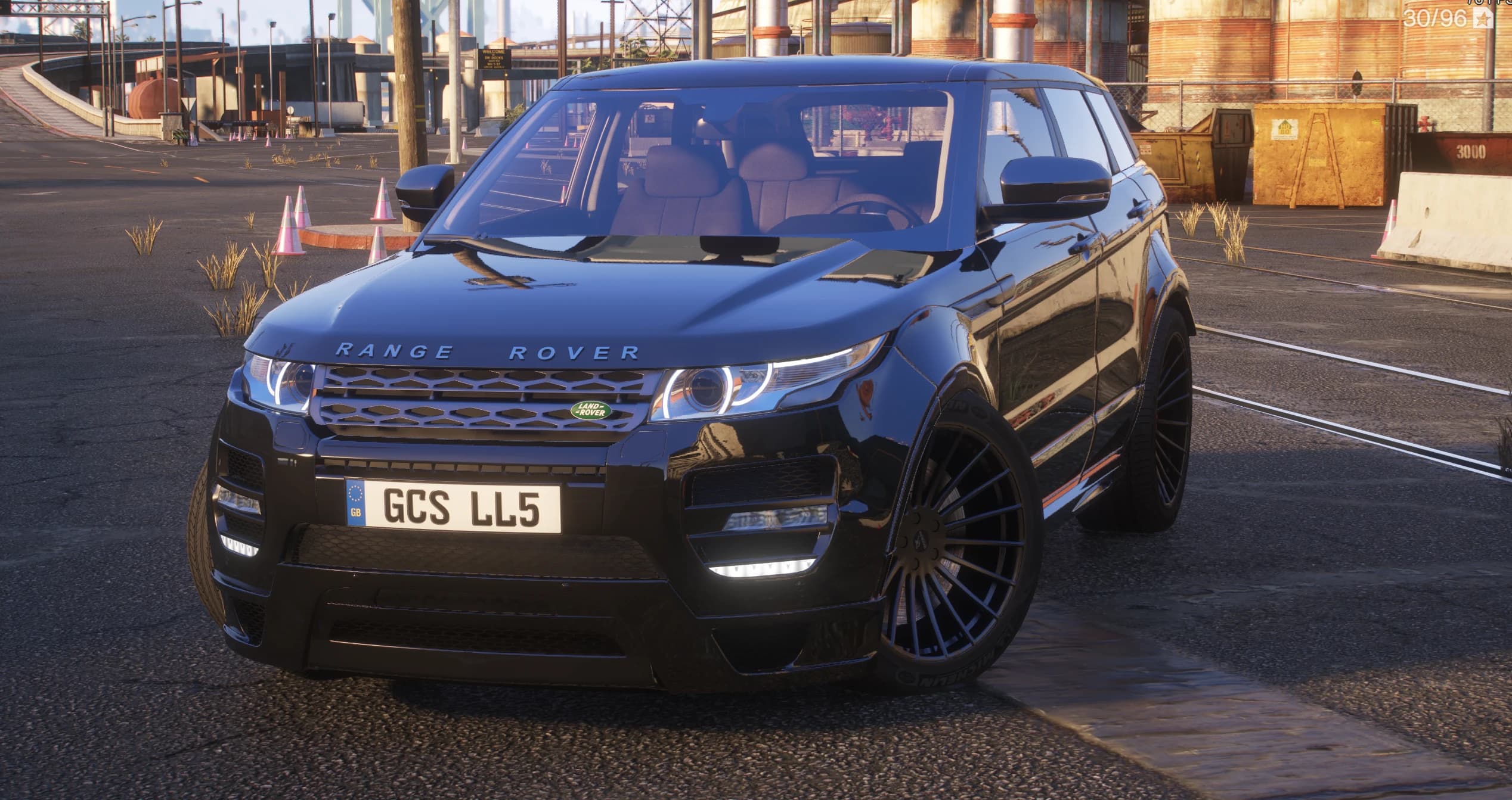 Frontal del Range Rover Evoque negro con el kit de carrocería ancha Hamann, faros de halo y llantas negras multirradio en un polígono industrial