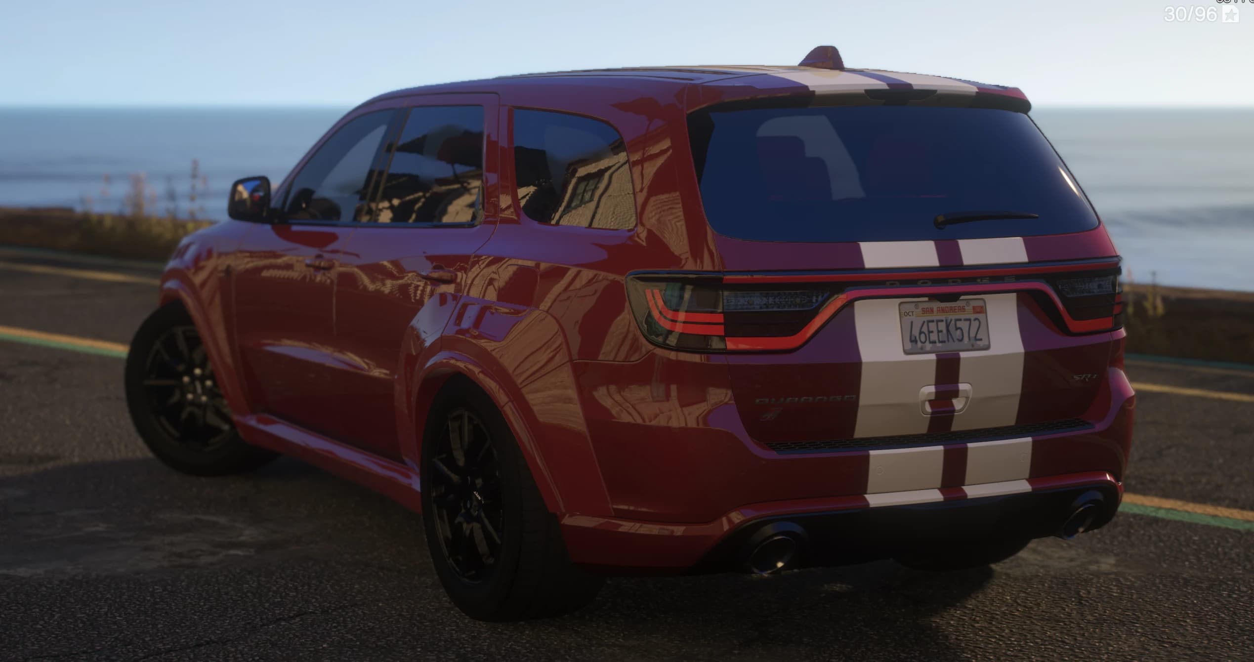 Tres cuartos trasero del Durango rojo en una carretera costera, con la barra de luz LED de ancho completo y el rótulo 'DODGE', las franjas blancas sobre el portón, los escapes dobles y una matrícula de San Andreas 46EEK572