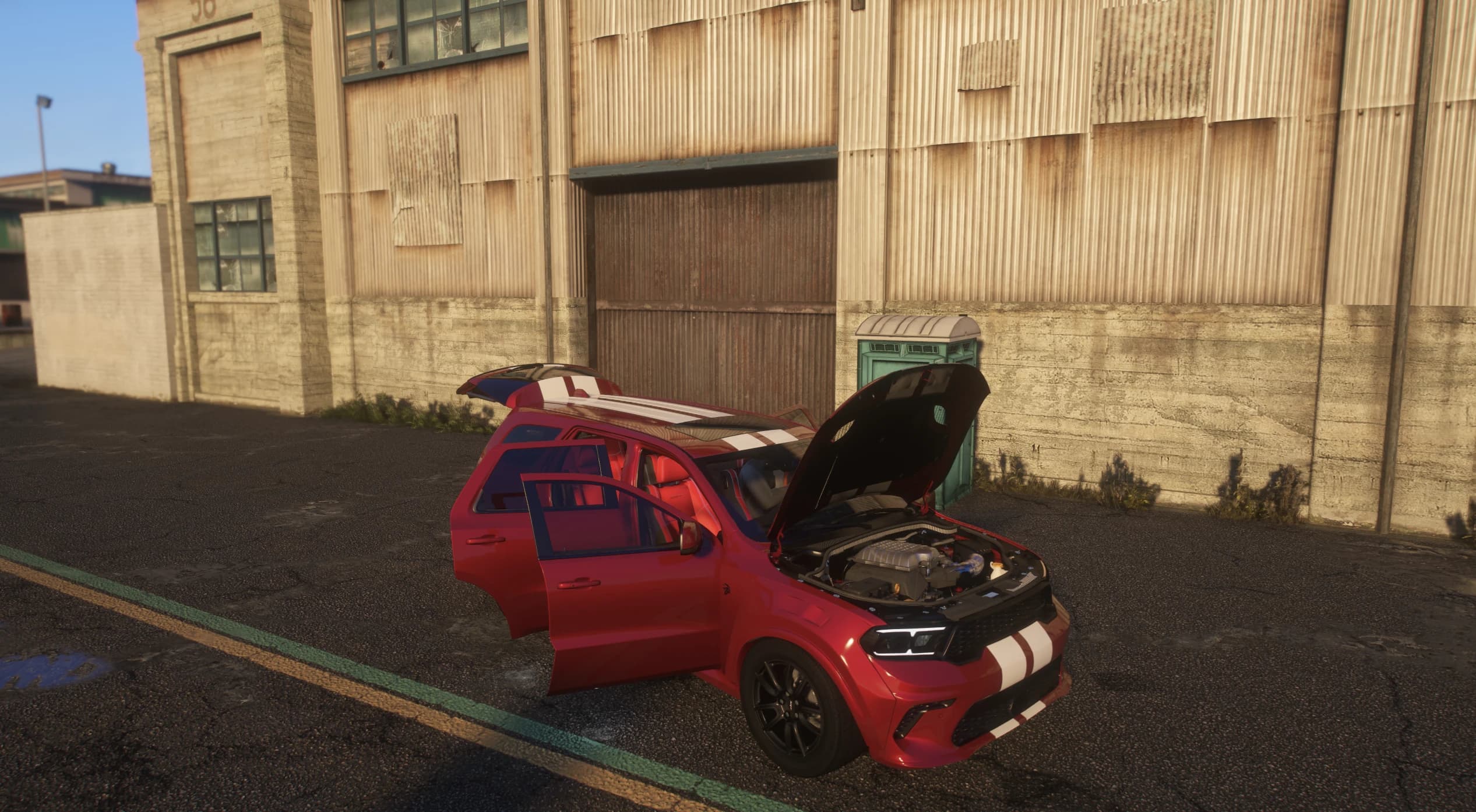 Durango rojo con el capó y las dos puertas izquierdas abiertos frente a una nave desgastada, mostrando el vano motor HEMI sobrealimentado y el interior en rojo y negro