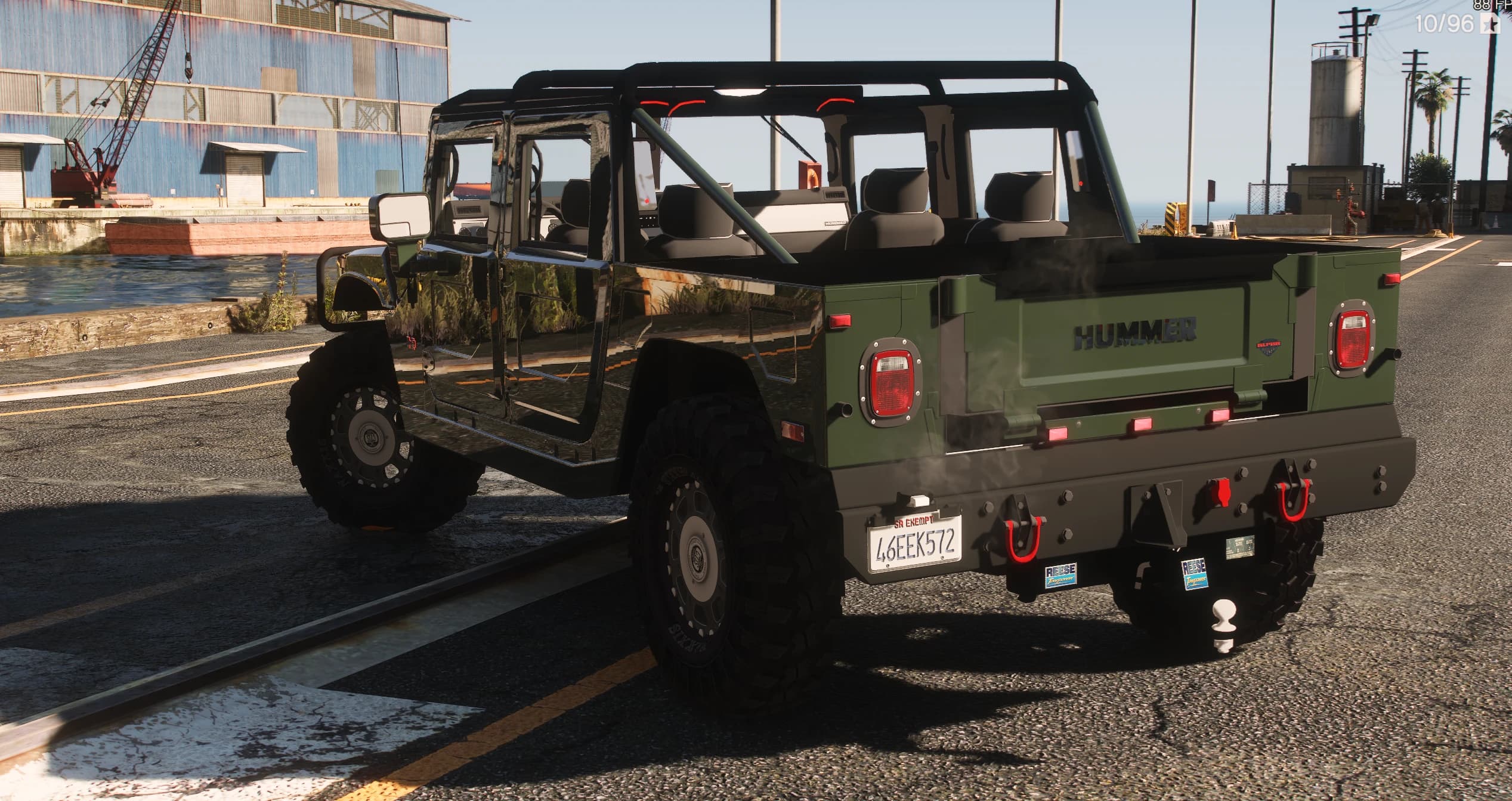 Tres cuartos trasero del H1 verde con el rótulo HUMMER en el portón, pilotos rojos, ganchos de remolque y bola de enganche en el paragolpes trasero, y la cabina descubierta con los asientos a la vista