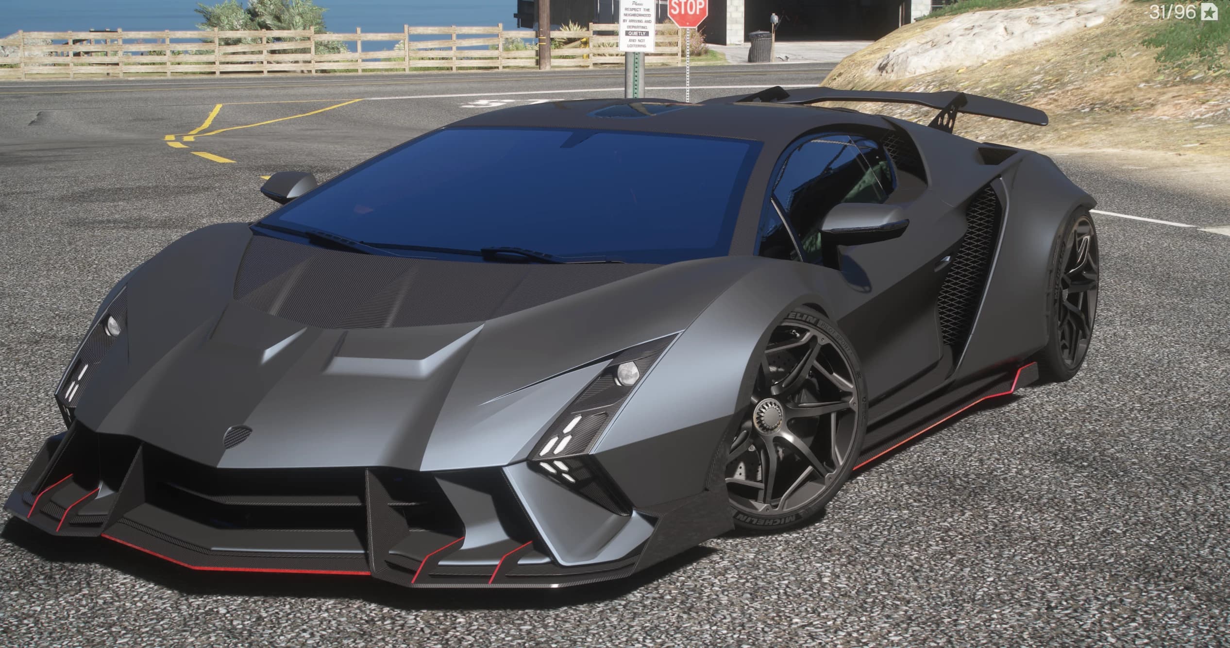 Vista frontal en tres cuartos del Lamborghini Invencible gris mate con el splitter perfilado en rojo, canards de carbono, toma de aire en el techo y alerón trasero en una carretera costera