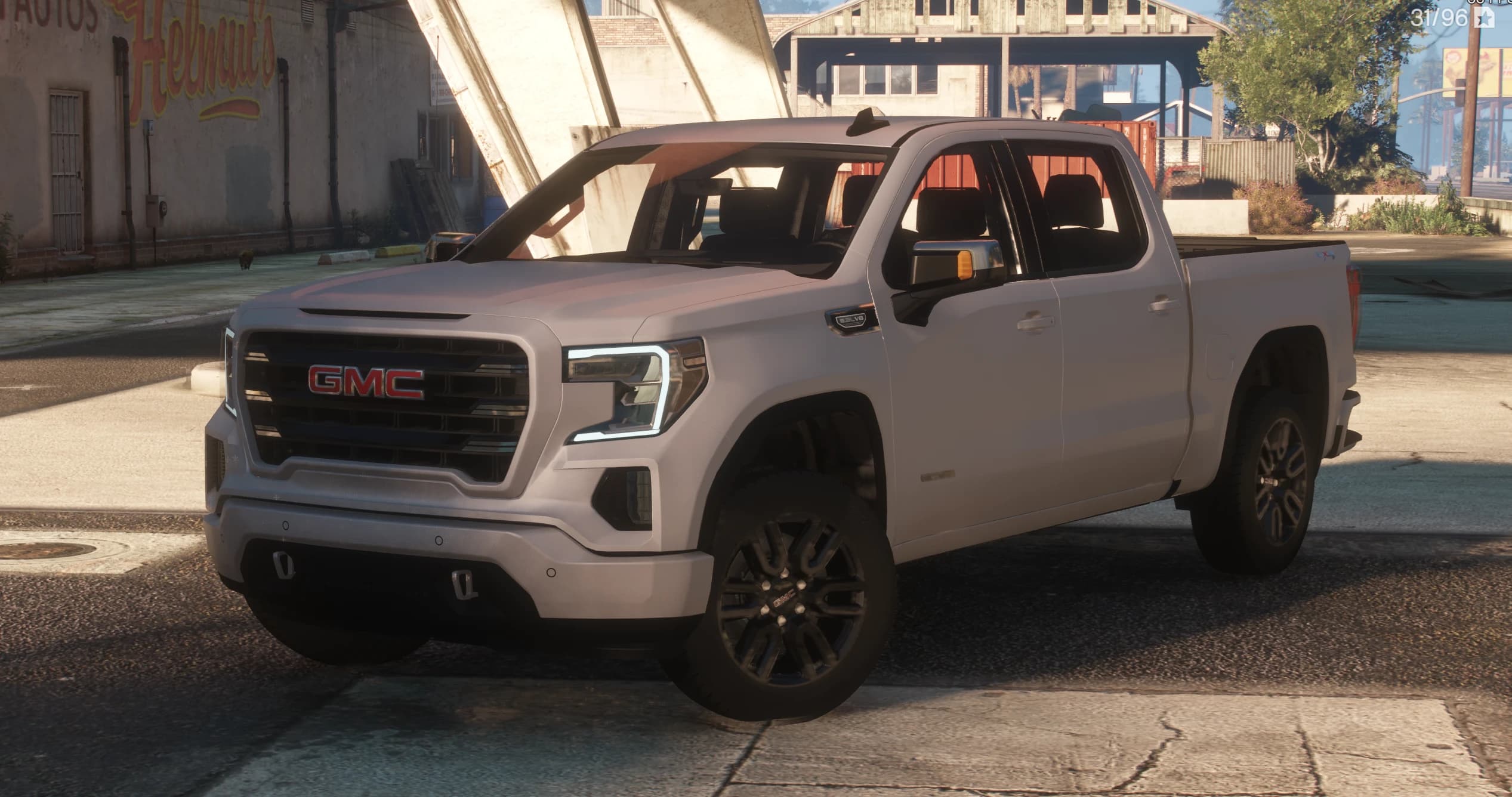 Vista frontal en tres cuartos de la GMC Sierra AT4 de doble cabina en blanco, con el logo rojo GMC, luces diurnas en forma de C y el emblema 6.2 V8 en el capó