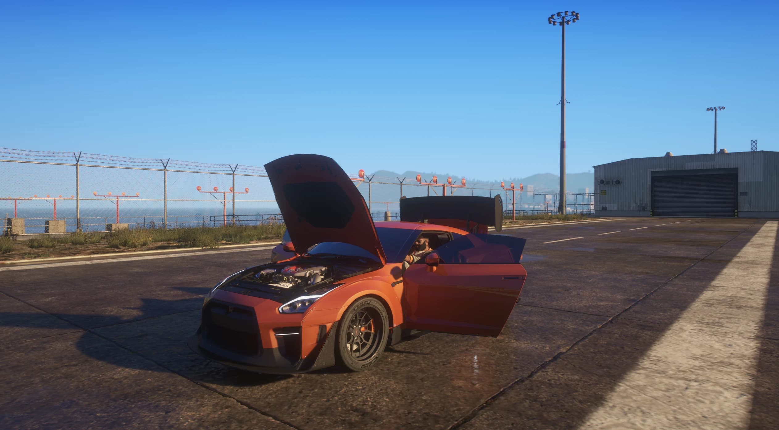 El GT-R aparcado en el hormigón del aeródromo con el capó abierto sobre el V6 biturbo y las dos puertas abiertas