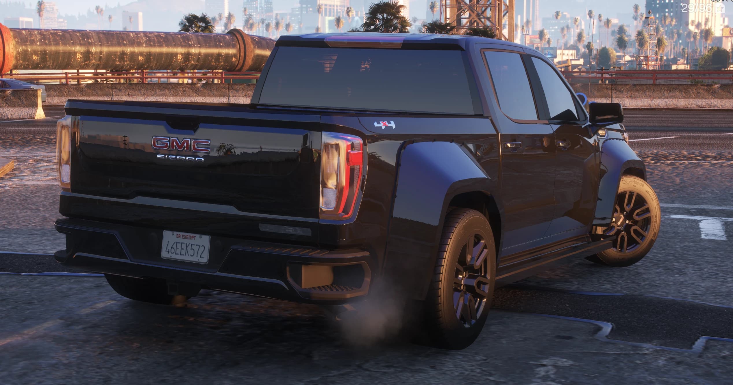 Tres cuartos trasero del GMC Sierra con el rótulo GMC SIERRA en el portón, una calcomanía 4x4 en la caja, pasos de rueda widebody traseros y el perfil de Los Santos al fondo